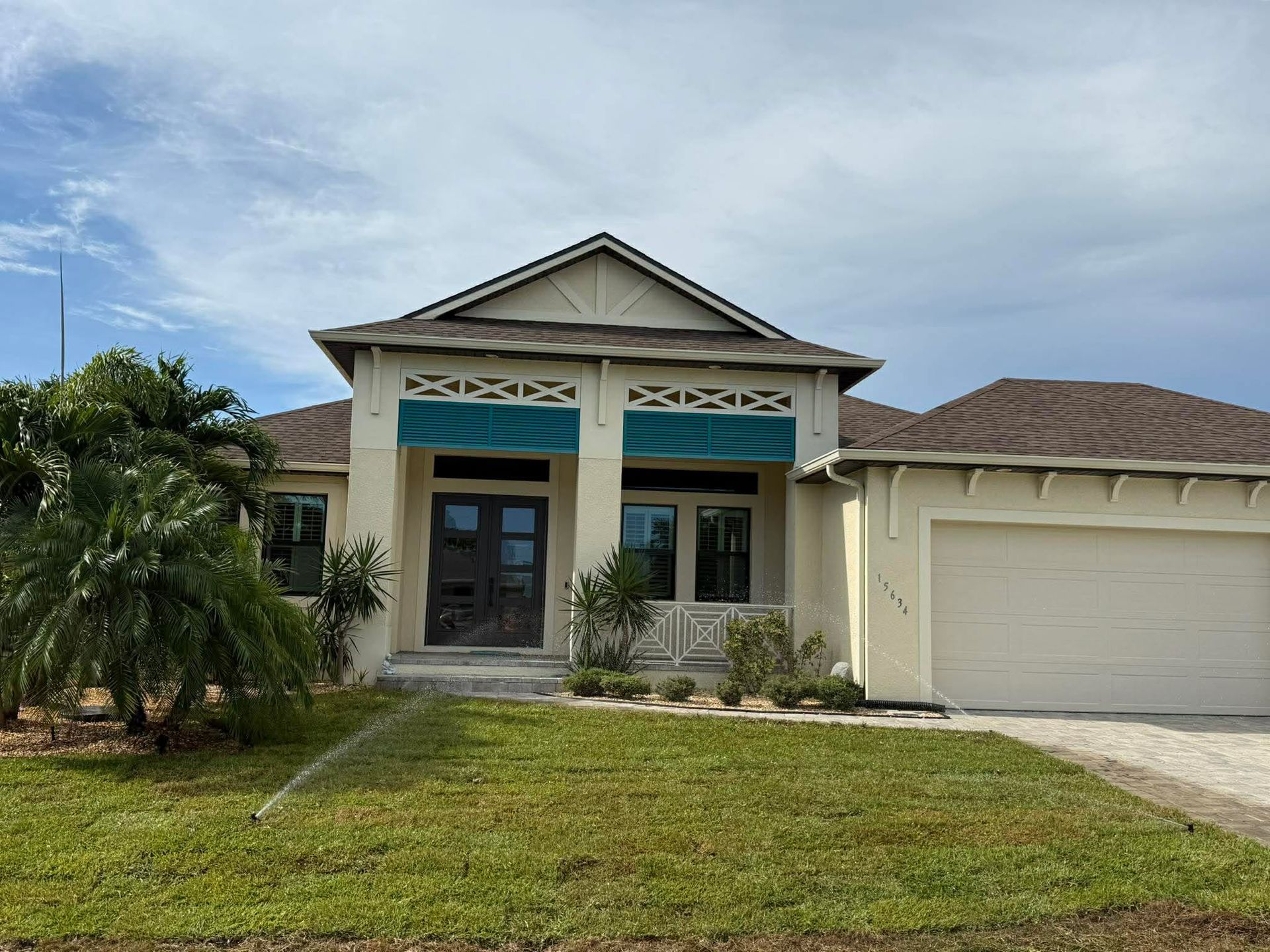 Single-story beige house with a two-car garage, front lawn, and palm tree under a cloudy sky