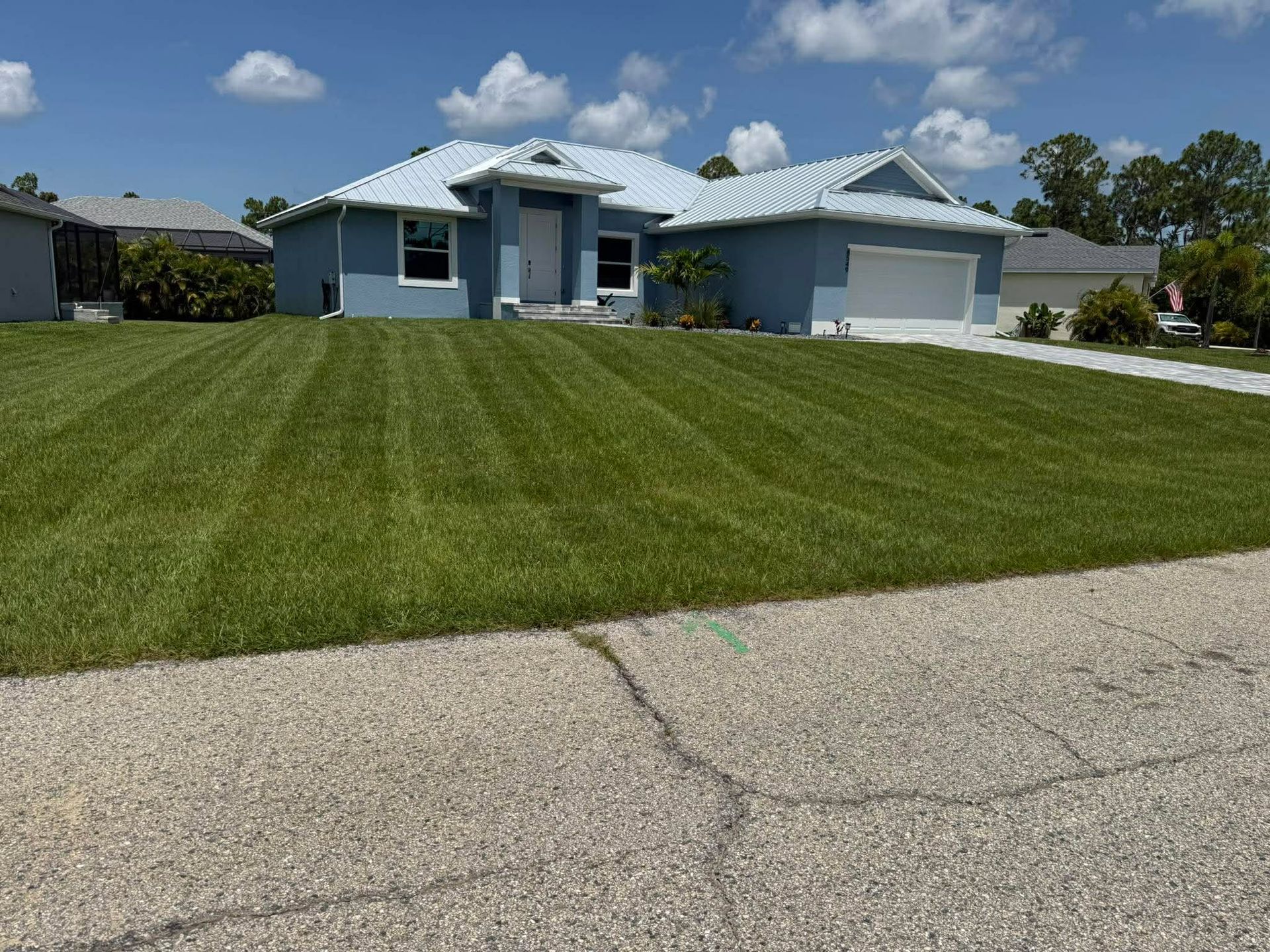 Single-story blue house with a white garage and large green lawn under a partly cloudy sky