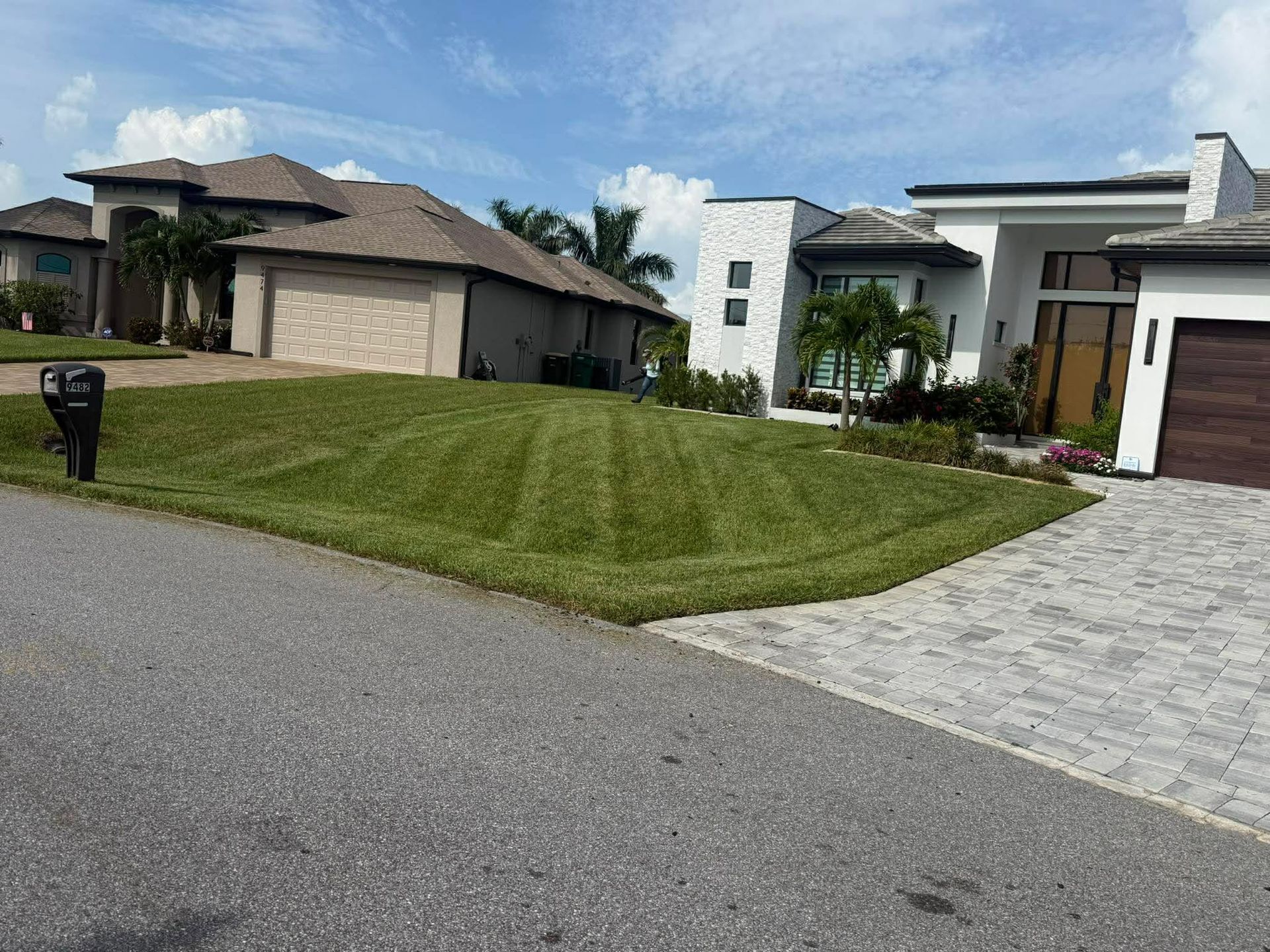 Lawn being mowed with a riding mower, creating striped patterns in the green grass on a sunny day.