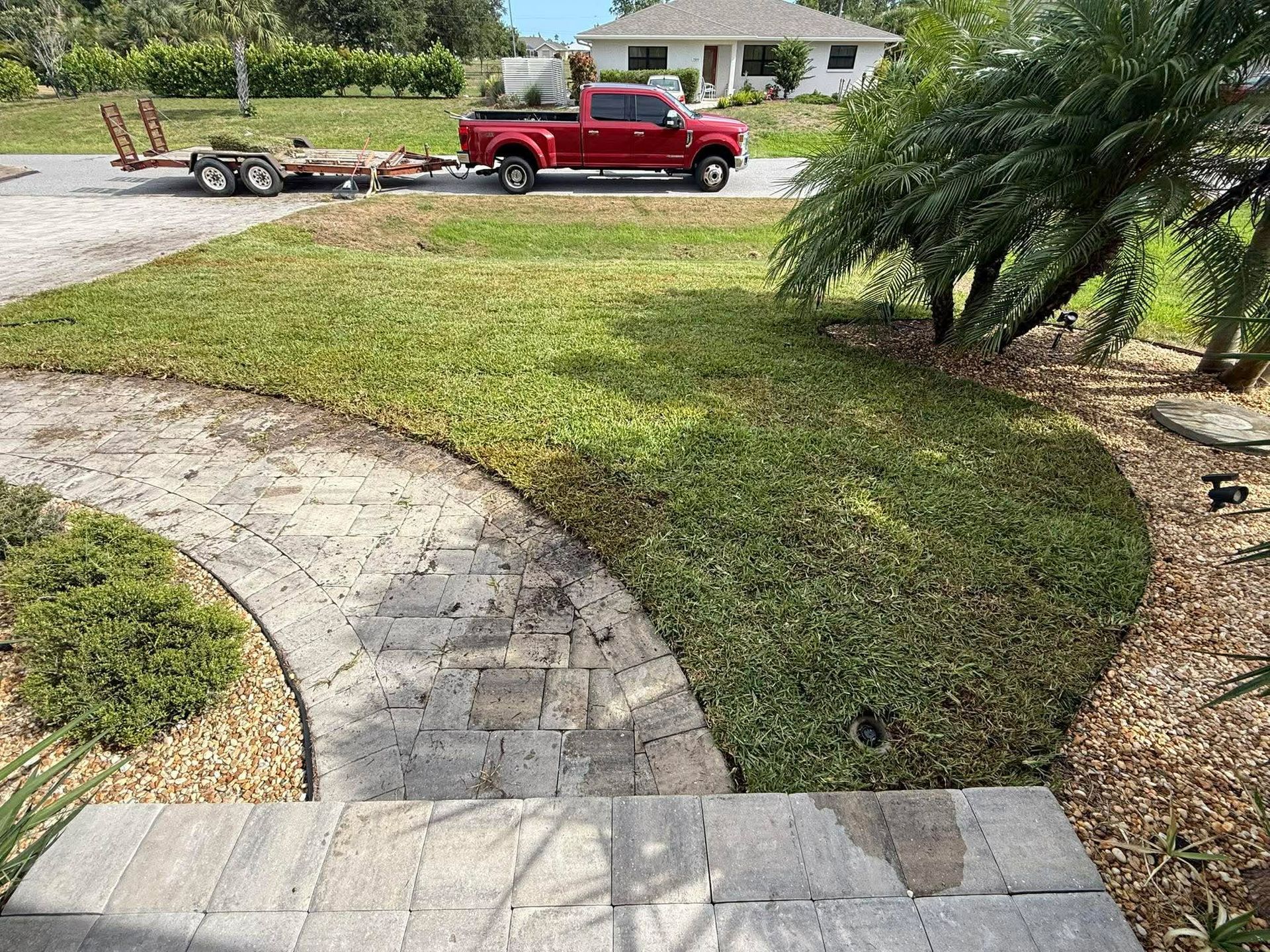 Red pickup truck towing a small trailer parked by a curved stone walkway in a grassy yard