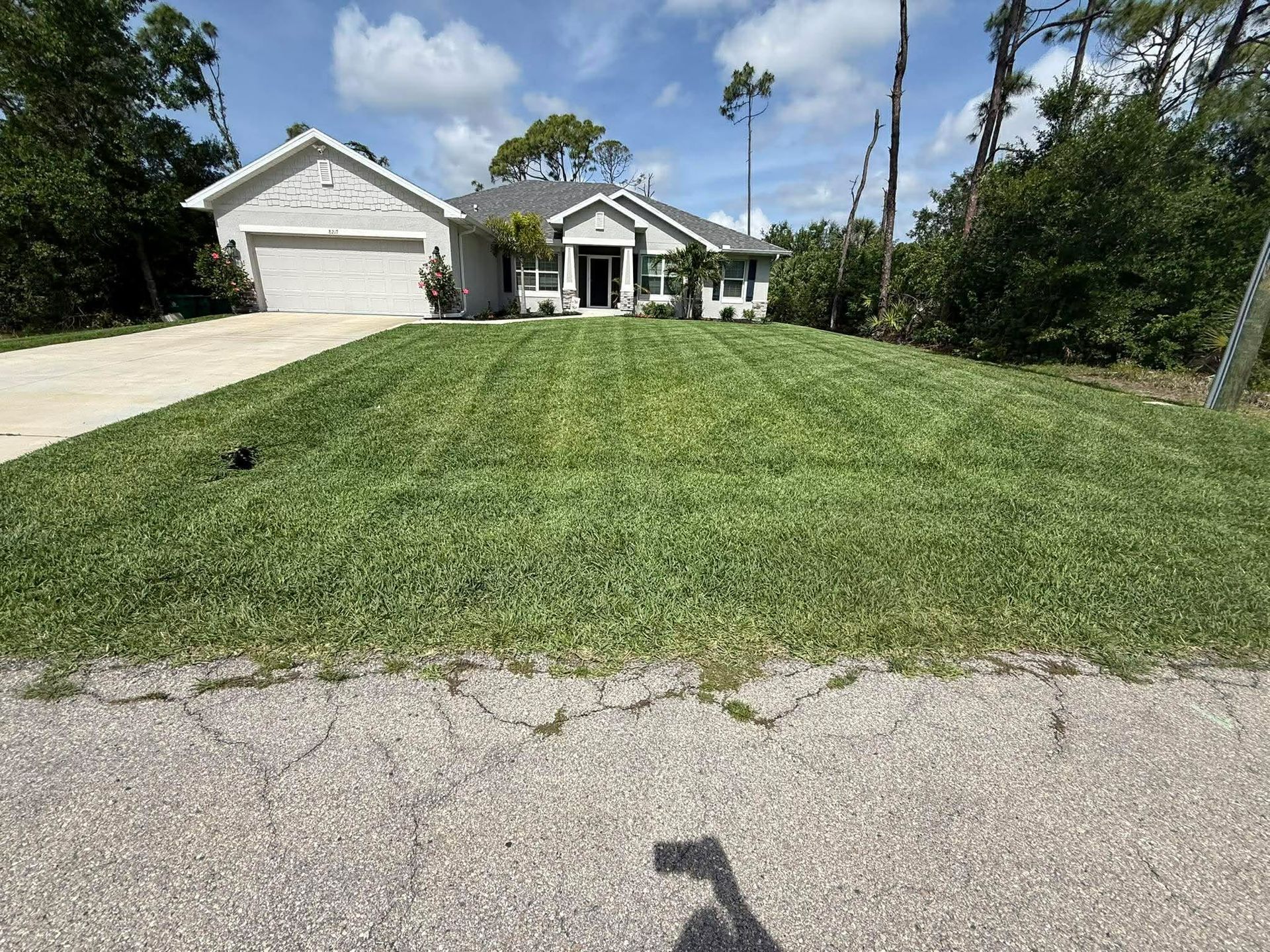 Suburban house with a two-car garage, white columns, and a large sloped front lawn under a clear sky