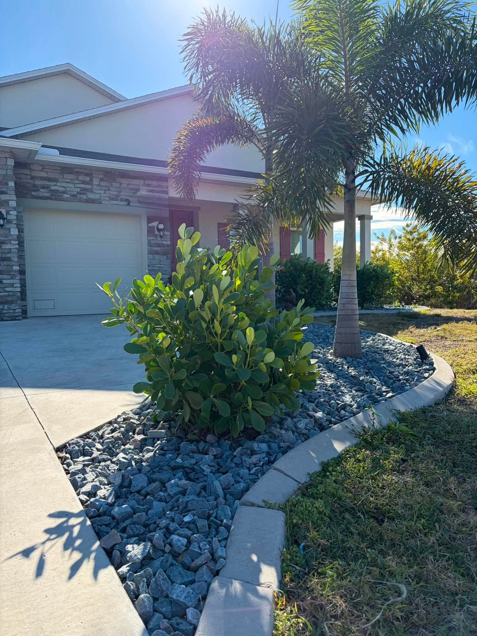 Tan stucco house with a tile roof, arched entryway, brick driveway, and manicured landscaping.