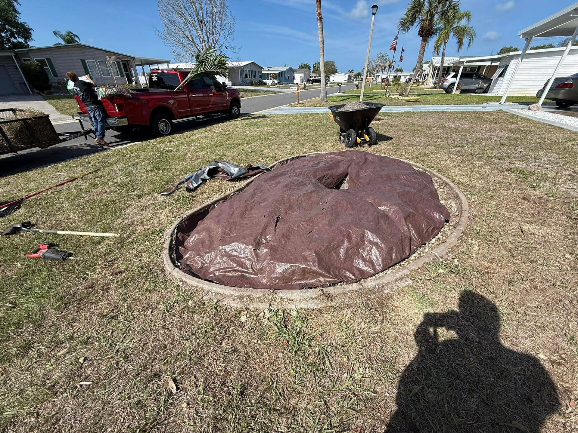 Backyard with a large covered fire pit, red truck, palm trees, and a grill on a sunny day