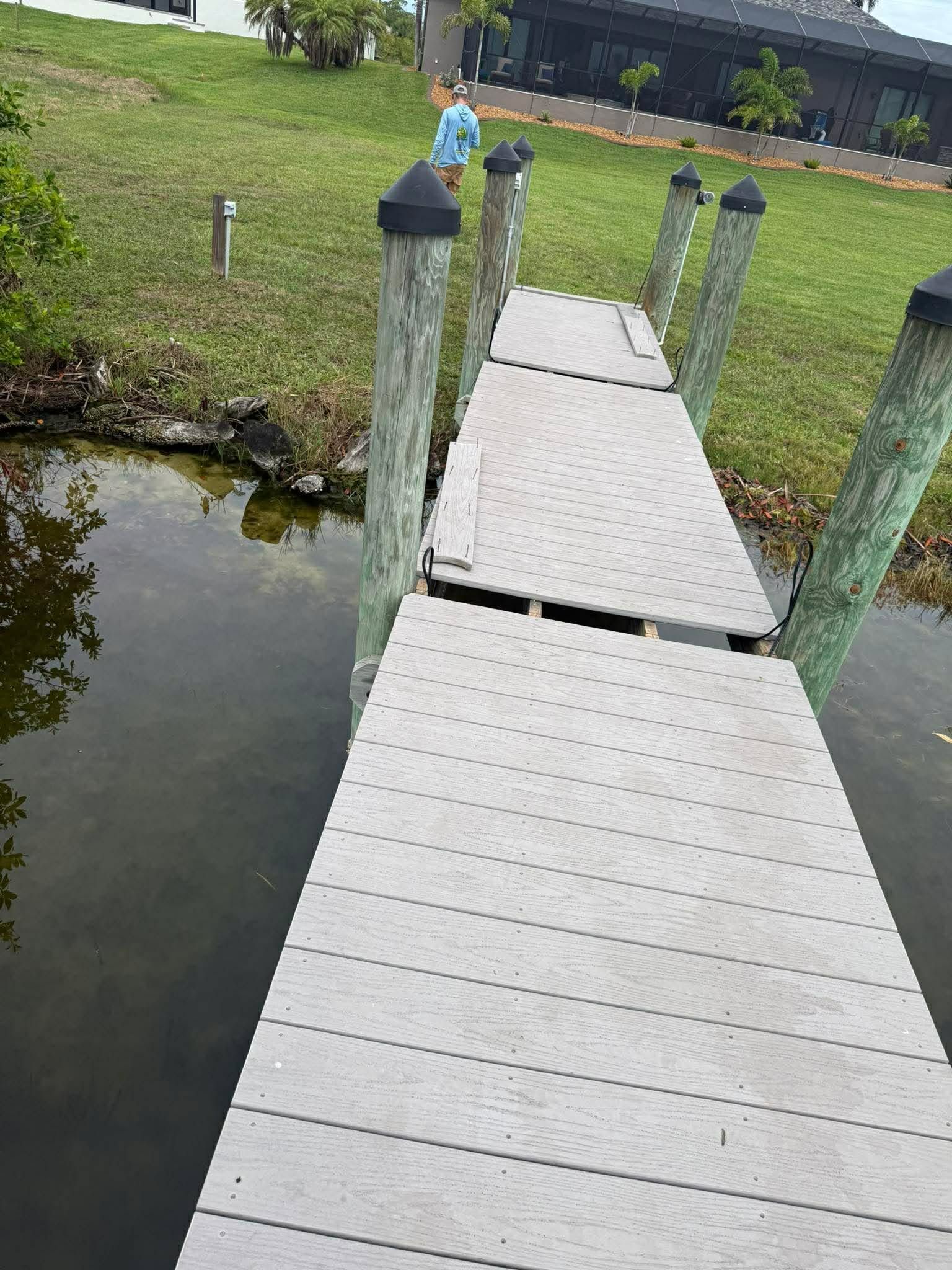 Wooden dock over a pond leading to a grassy shore with a person standing near the end