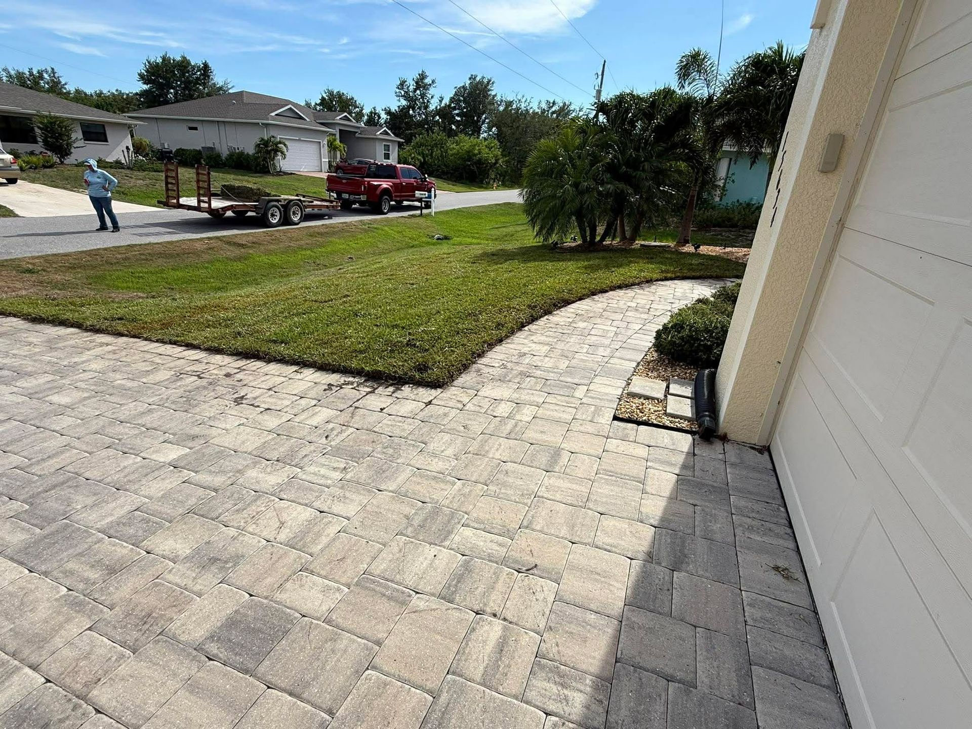 Driveway and front lawn with a person walking near a red pickup truck on a sunny suburban street.