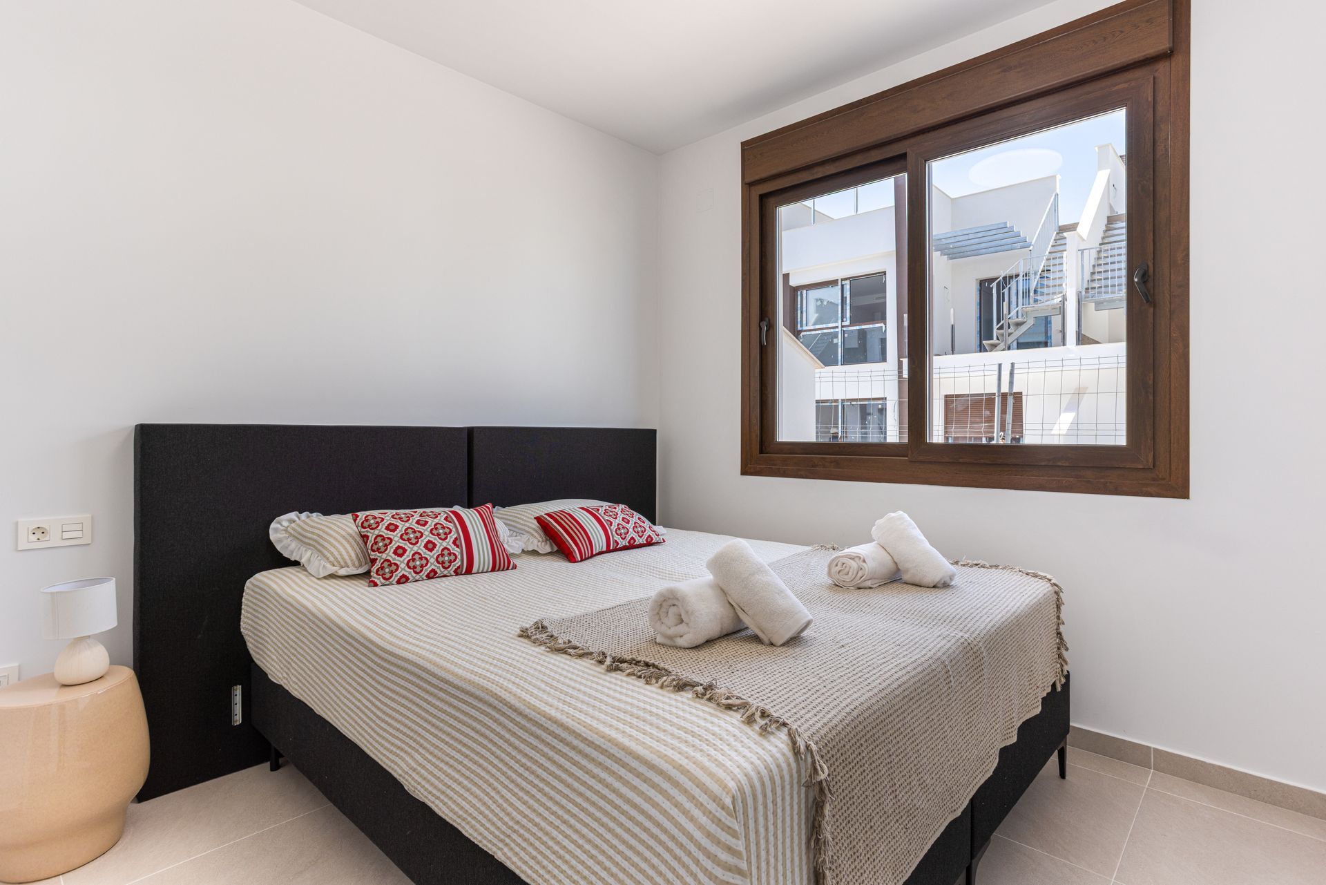 Bright bedroom with a bed, patterned pillows, and a window overlooking buildings