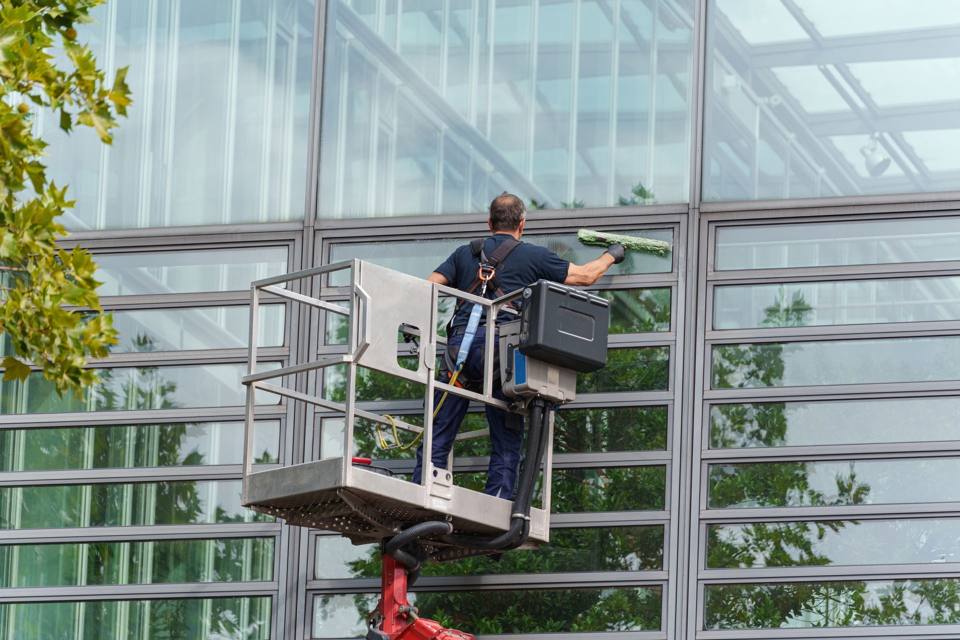 Worker on a lift cleaning a glass building facade.