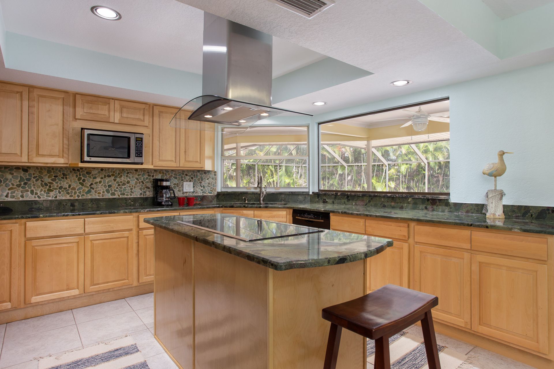 Bright kitchen with wood cabinets, granite island, stainless range hood, and a stool by the counter