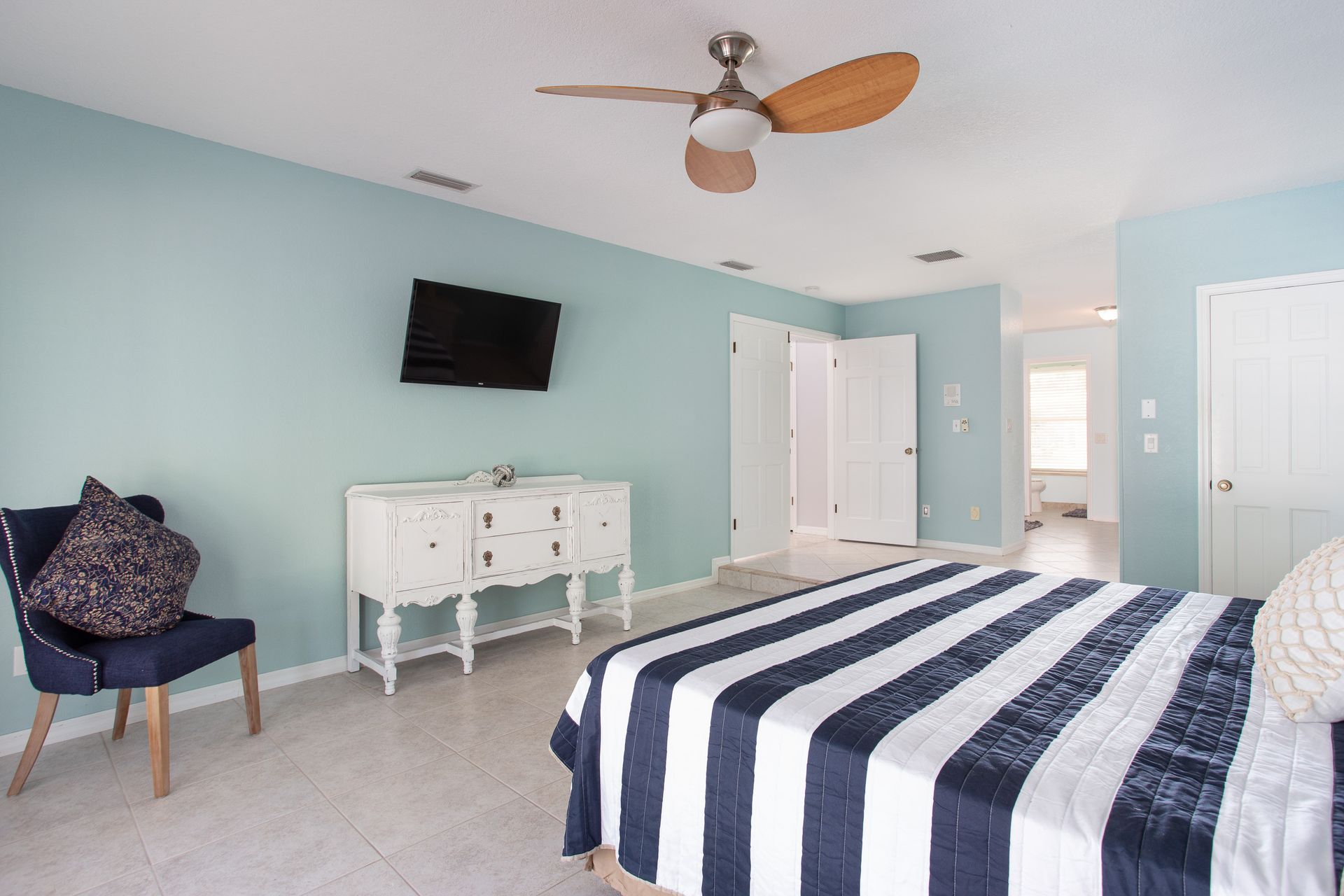 Spacious bedroom with striped bedspread, wall-mounted TV, mint walls, and ceiling fan