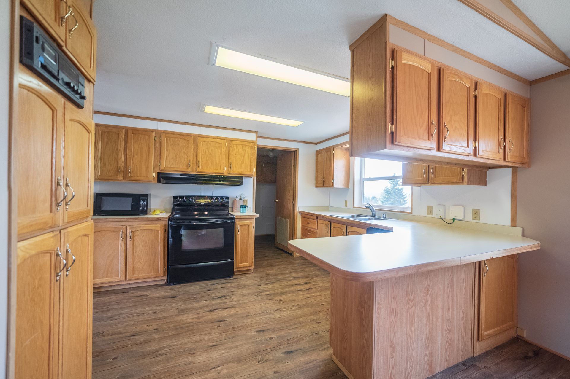 Kitchen with wooden cabinets, black stove, light countertops, and a peninsula island