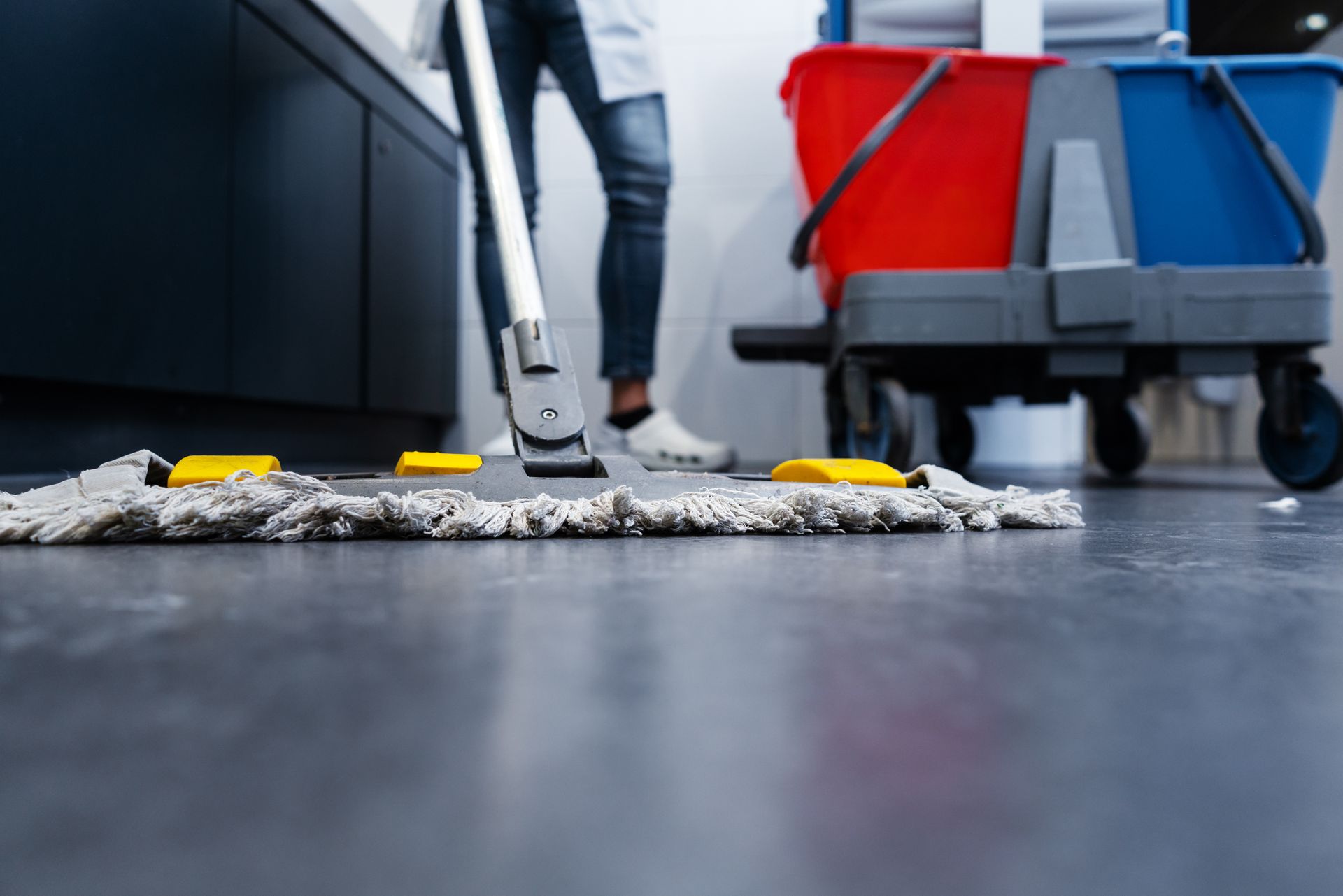 Professional cleaner mopping commercial floor with janitor cart and buckets nearby. Professional cleaner mopping commercial floor with janitor cart and buckets nearby.