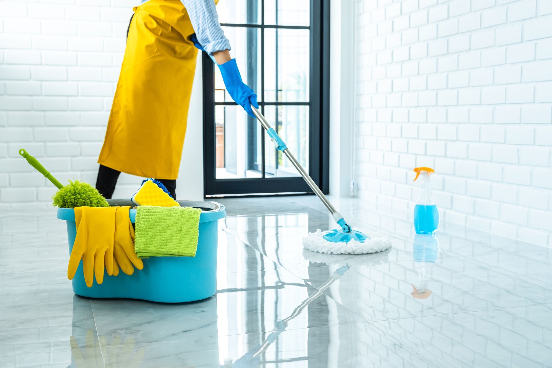 Person mopping a bright kitchen floor with bucket, gloves, and cleaning supplies