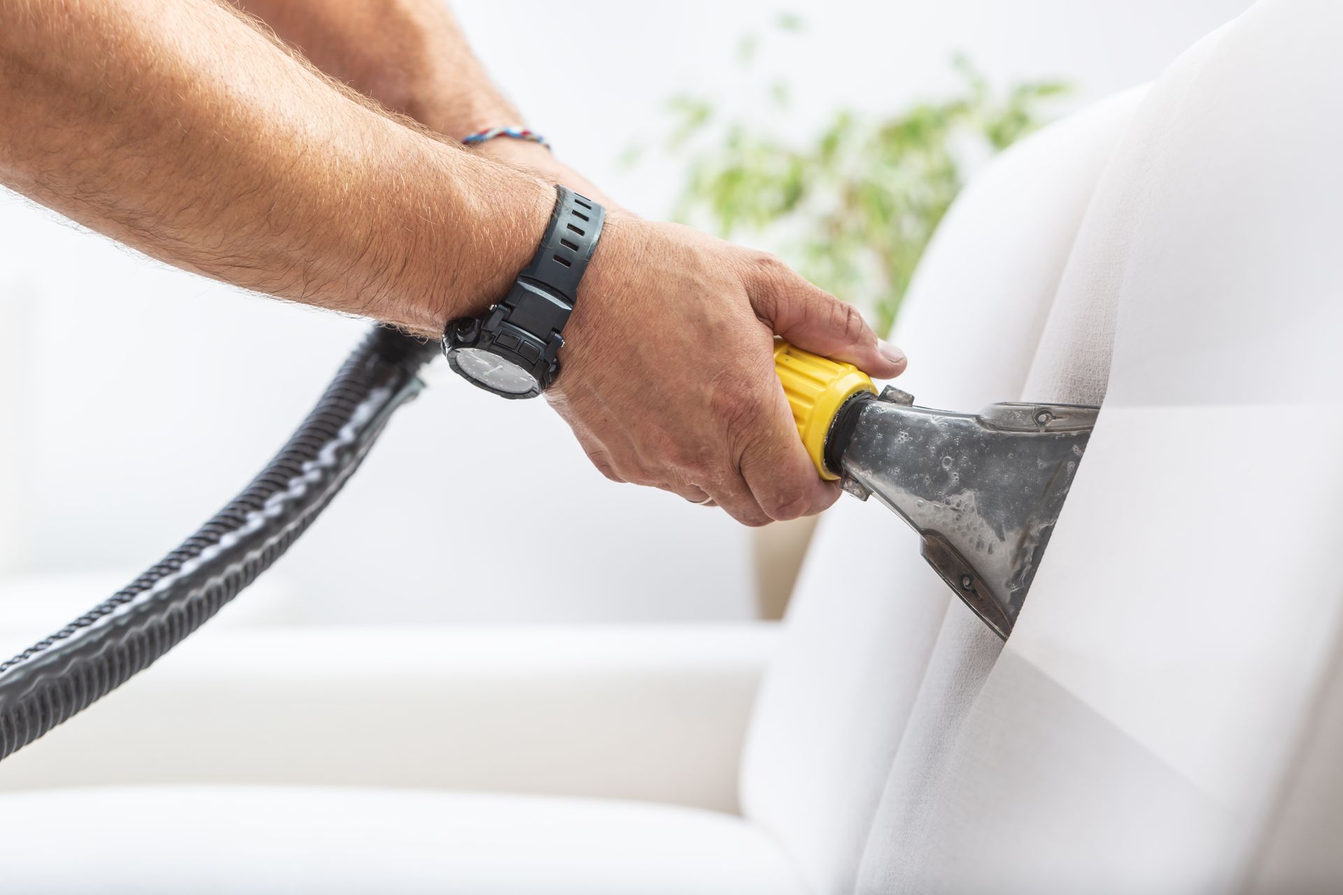 Hand holding a steam-cleaning nozzle on a white couch cushion