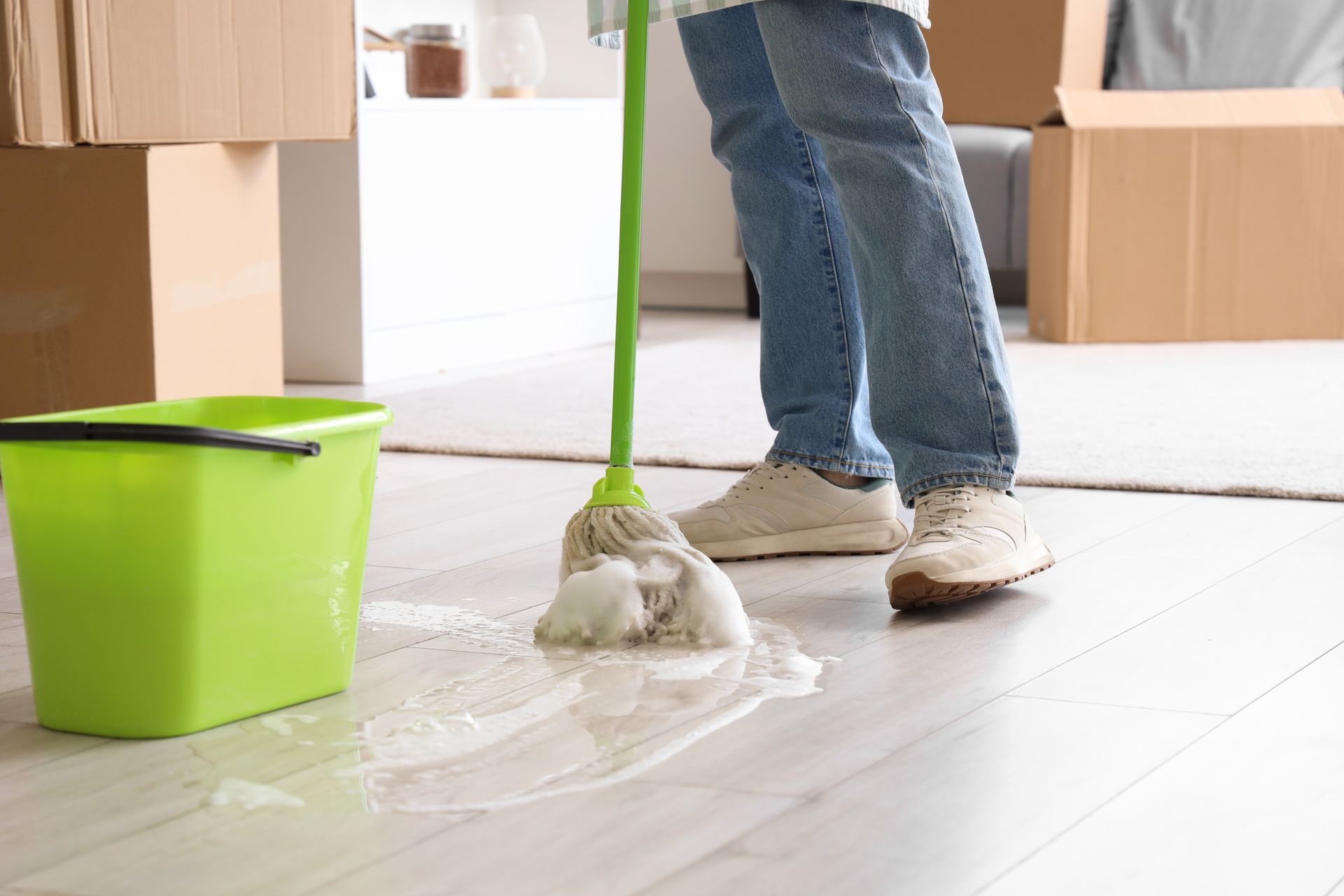 Person mopping a white floor with a green bucket beside cardboard boxes