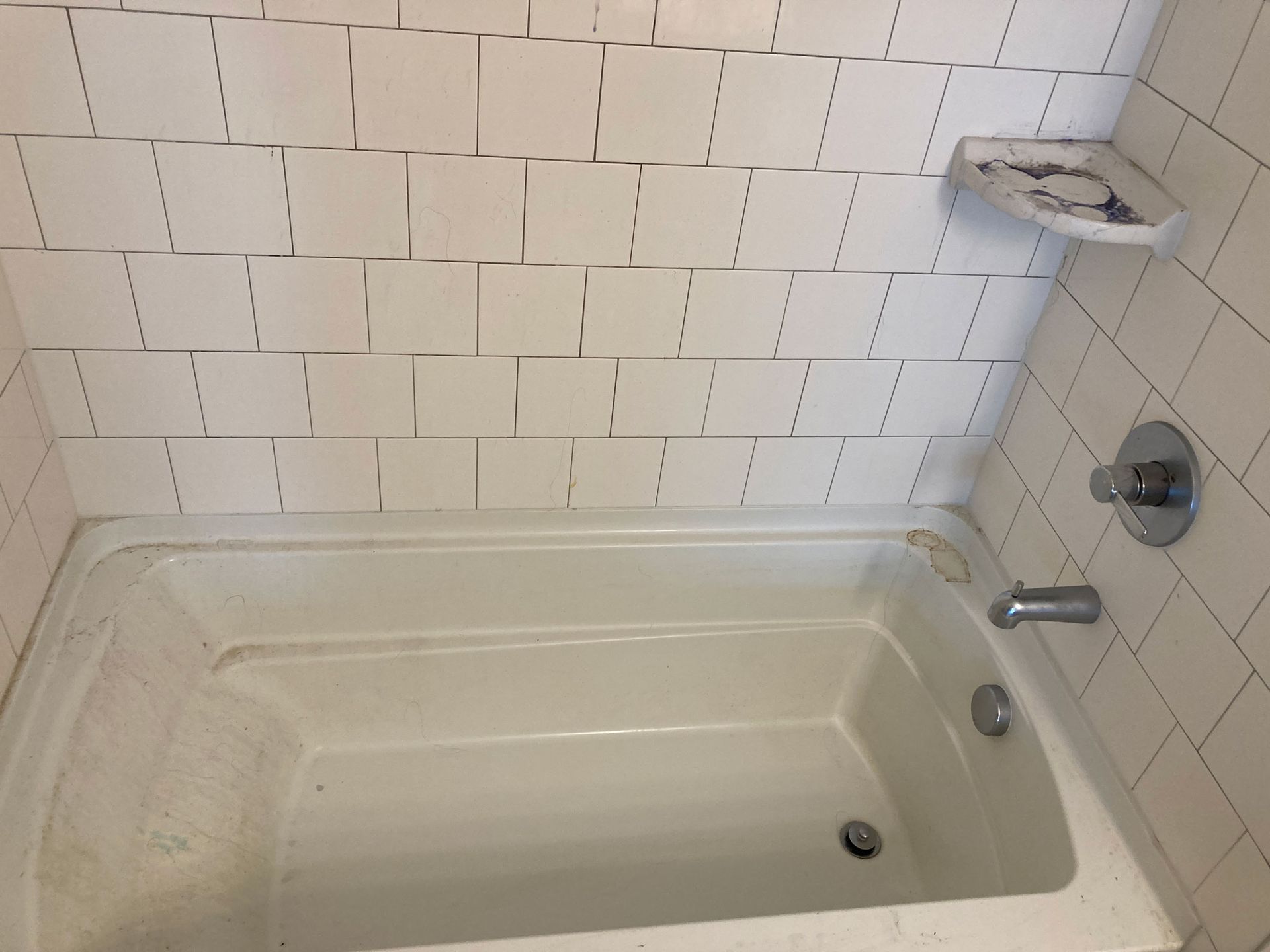 Bathtub with beige tile walls, showerhead, faucet, and built-in soap dish in a bathroom