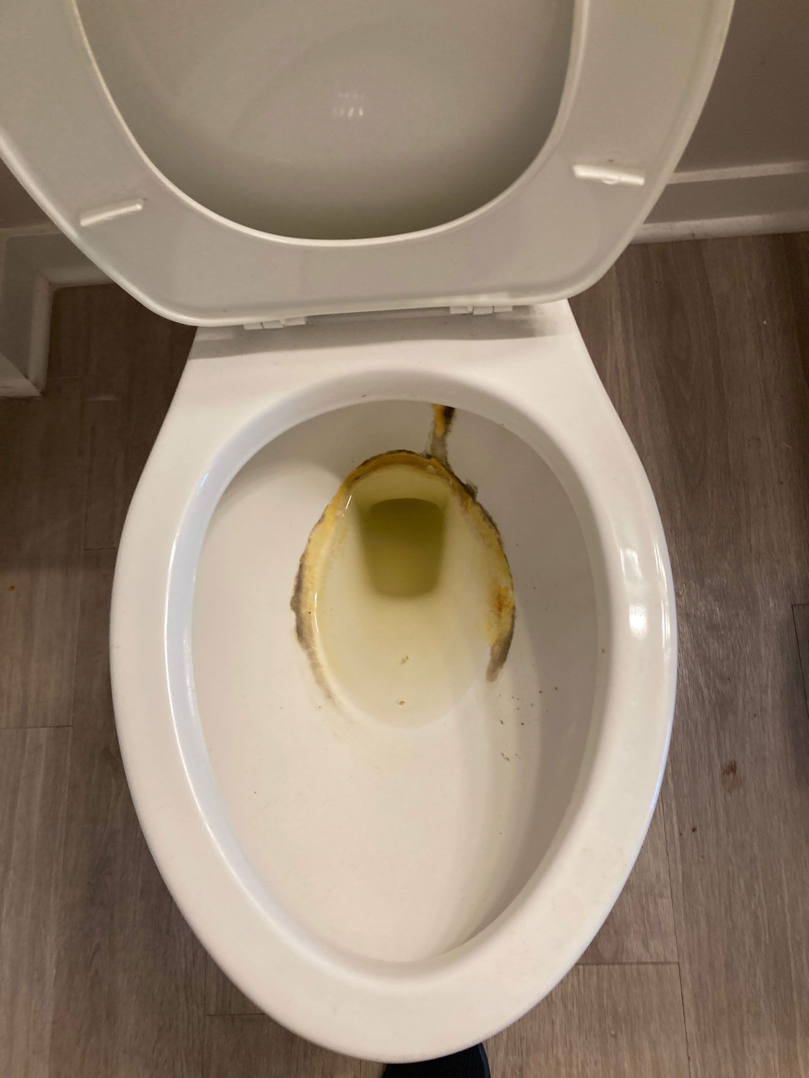 Open toilet bowl with yellowish liquid stain and residue inside