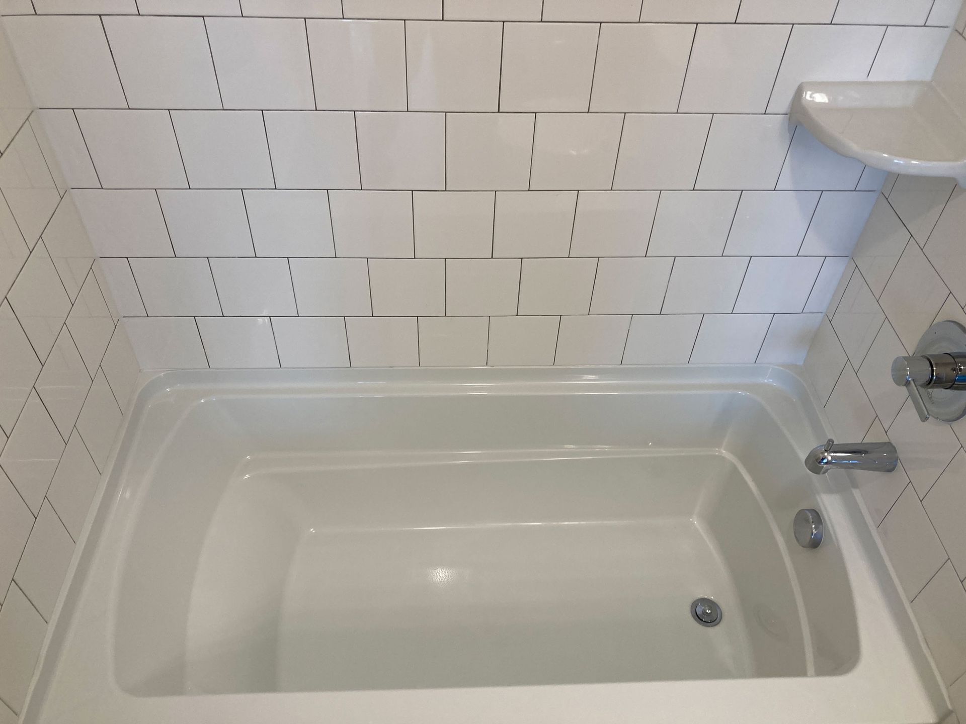 White bathtub and tiled shower wall in a bathroom