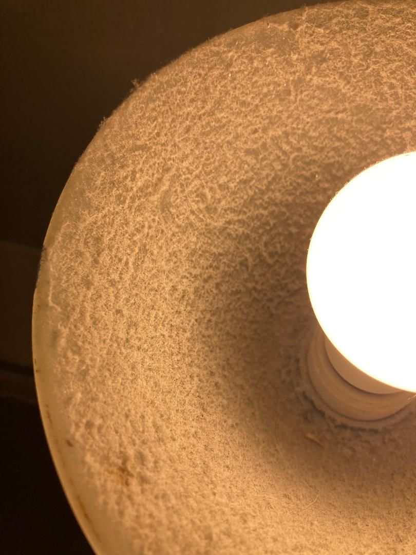 Close-up of a textured beige lampshade with a bright bulb glowing on the right