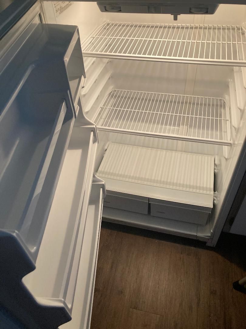 Open refrigerator with empty shelves and bins inside, viewed from the kitchen.