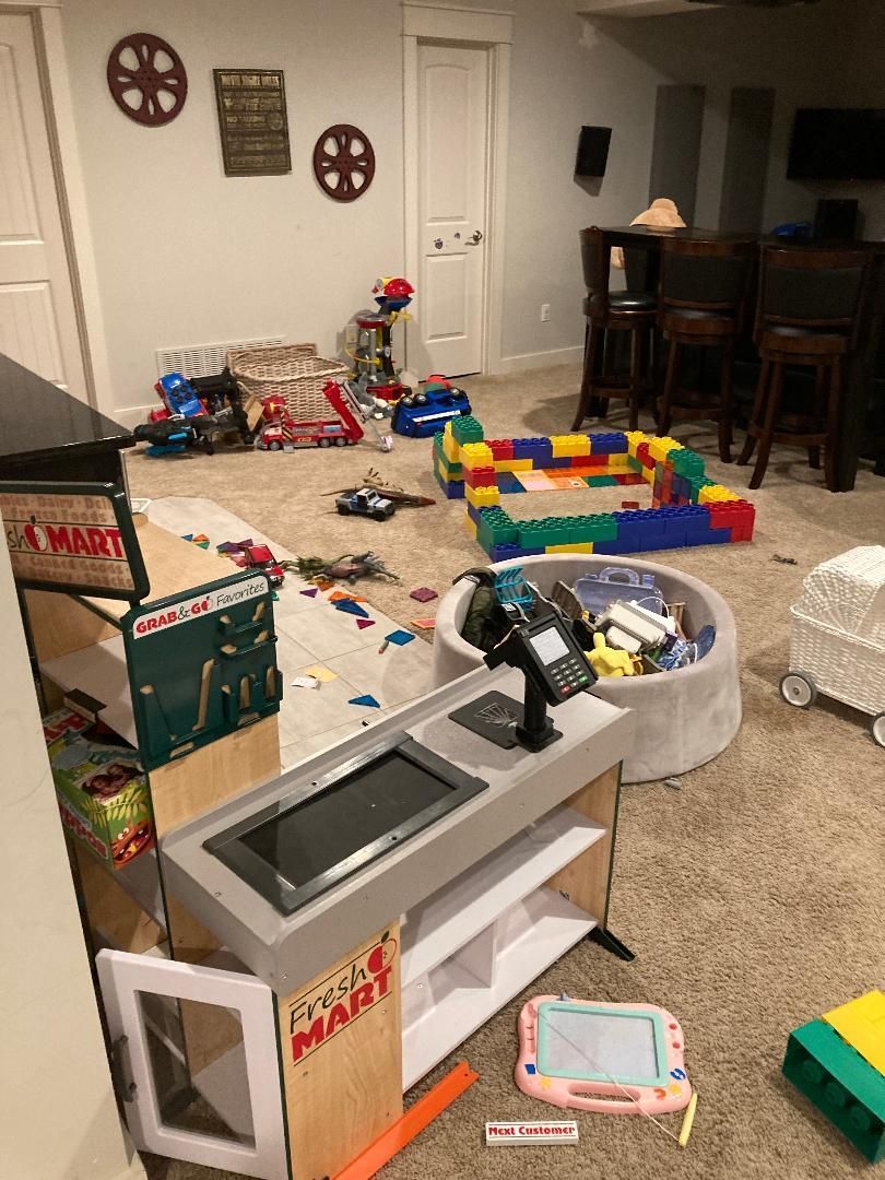 Messy playroom with scattered toys, colorful blocks, and a toy kitchen on the carpeted floor.
