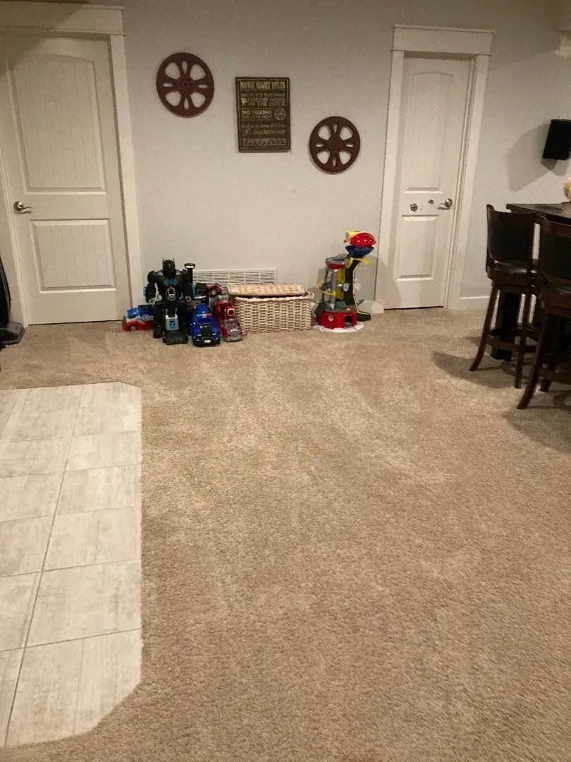 Living room with beige carpet, toy bins, wall decor, and piano on the right