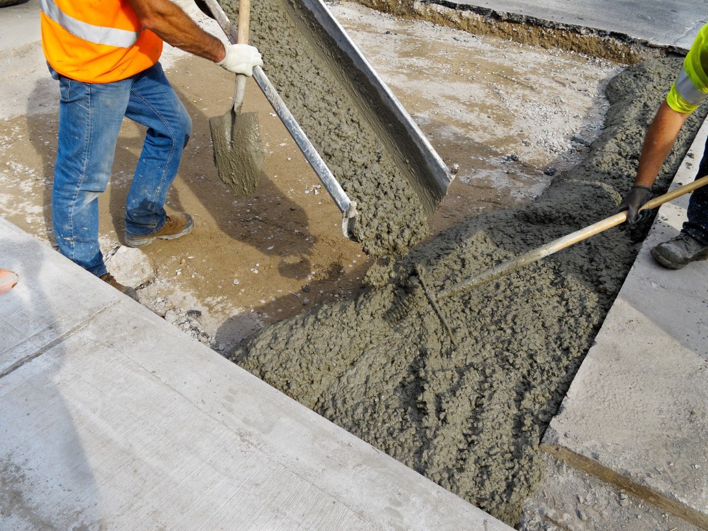 A man is pouring concrete into a hole with a shovel