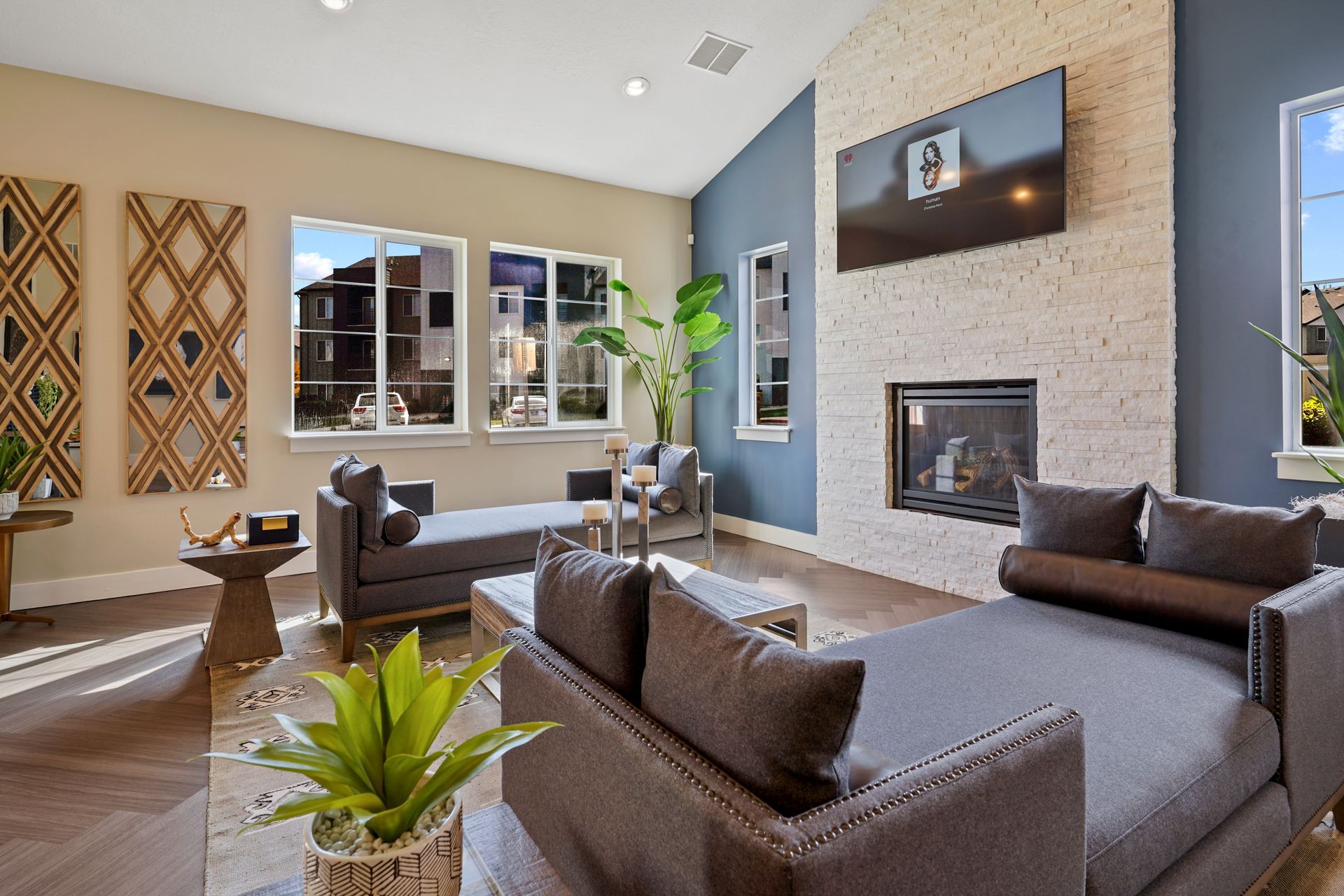 Clubouse with fireplace, TV, and gray couches at Wilshire Place, featuring apartments in West Jordan, UT. Beige brick wall, blue accent wall, and large windows.