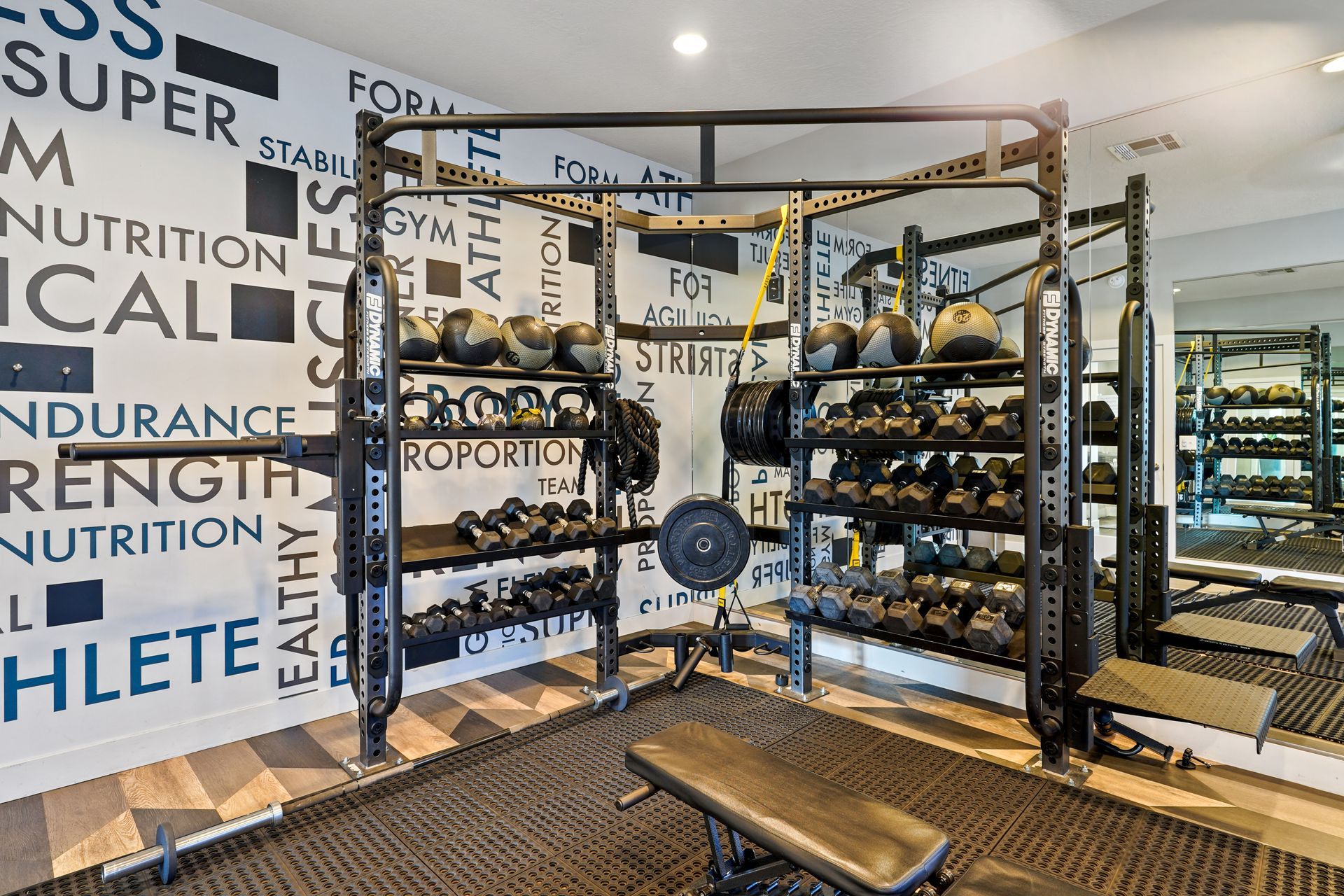 Gym with weight racks, dumbbells, kettlebells, bench, and motivational wall art at Wilshire Place, featuring apartments for rent in West Jordan, UT.