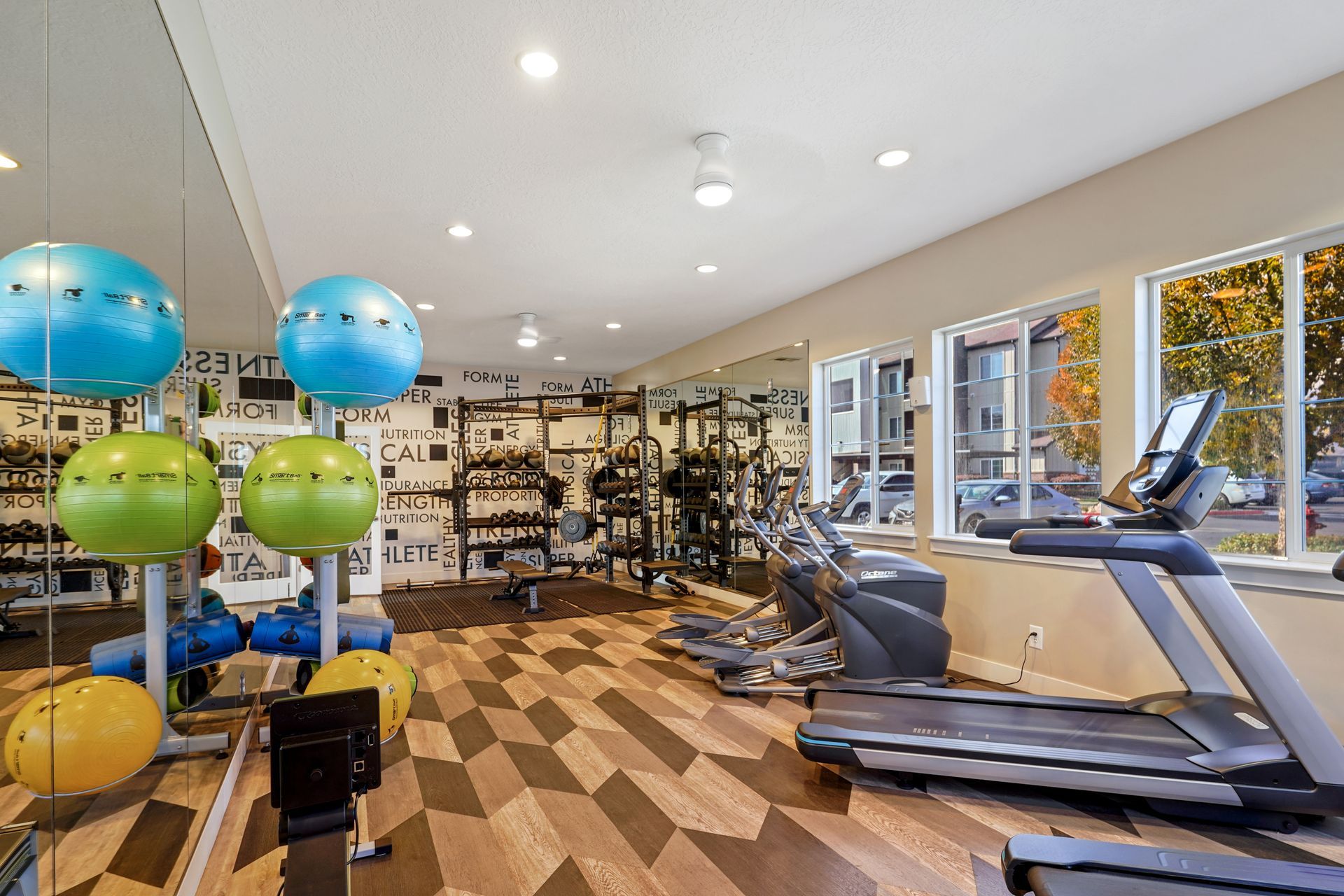 Gym with exercise equipment, including treadmills, weights, and stability balls; light-filled space at Wilshire Place, featuring apartments for rent in West Jordan, UT.