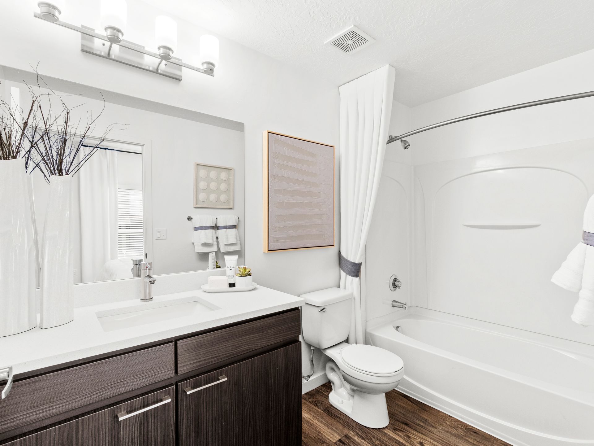 Modern bathroom with white sink, dark wood vanity, large mirror, toilet, and tub/shower at Wilshire Place, featuring pet-friendly apartments in West Jordan, UT.