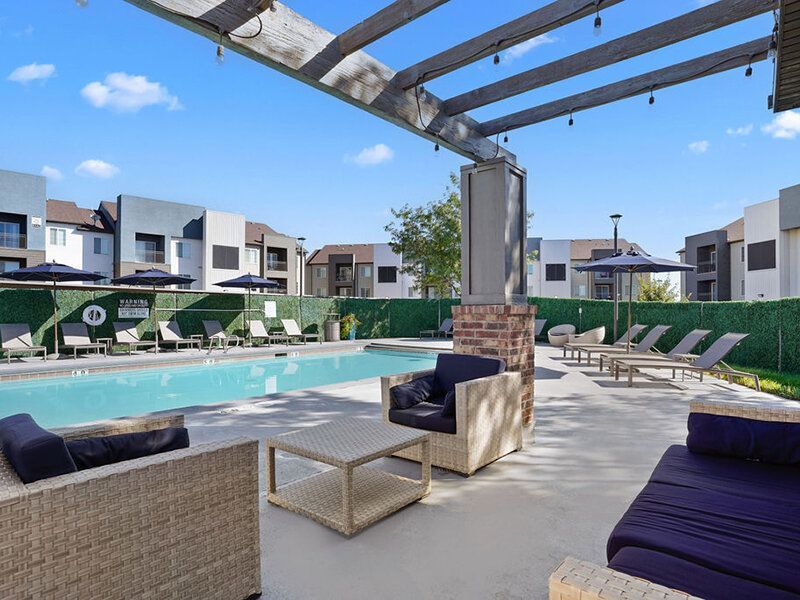 Outdoor pool area with lounge furniture under a pergola, adjacent apartment buildings at Wilshire Place, featuring apartments for rent in West Jordan, UT.