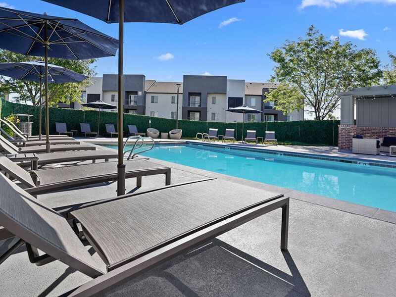 Poolside with lounge chairs and umbrellas, apartment building in background at Wilshire Place, featuring apartments in West Jordan, UT.