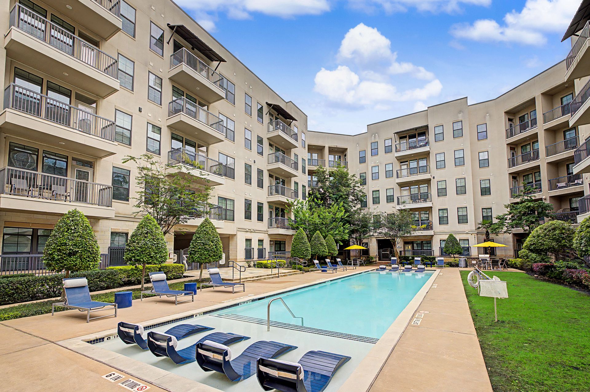 Apartment courtyard with a swimming pool, lounge chairs, and surrounding balconies under a blue sky at Olympus at Memorial, offering apartments in the Memorial area of Houston, TX.