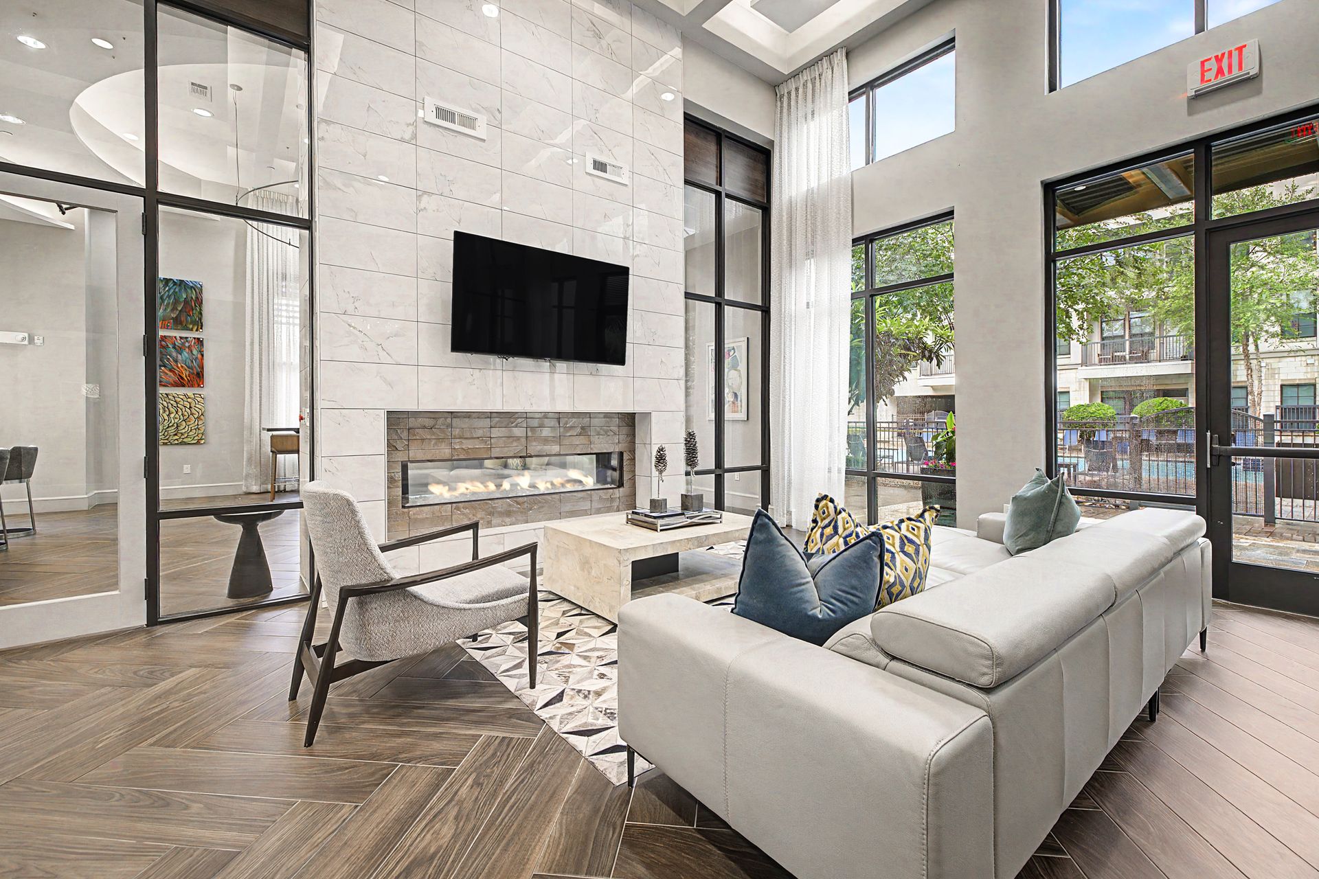 Modern clubhouse with white sectional sofa, wall-mounted TV, fireplace, and large windows at Olympus at Memorial, offering townhomes in Houston, TX.