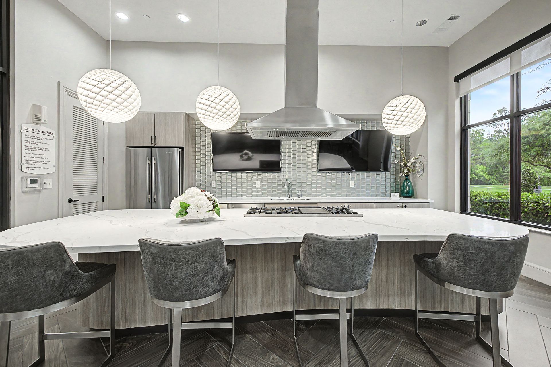Modern white kitchen with island, four gray stools, pendant lights, stainless appliances, and large windows at Olympus at Memorial, offering townhomes for rent in Houston, TX.