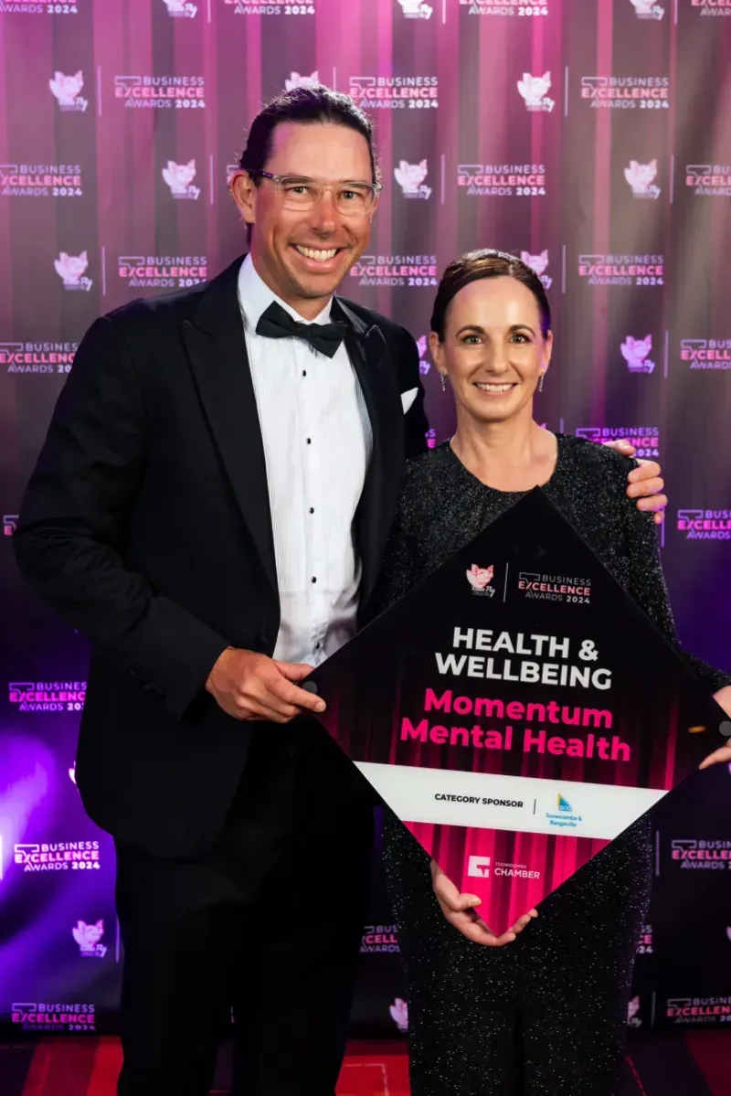 Chris Black and a woman are holding a health and wellbeing business excellence award for momentum mental health.