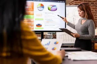 Presenter pointing at charts on a large screen during a business meeting