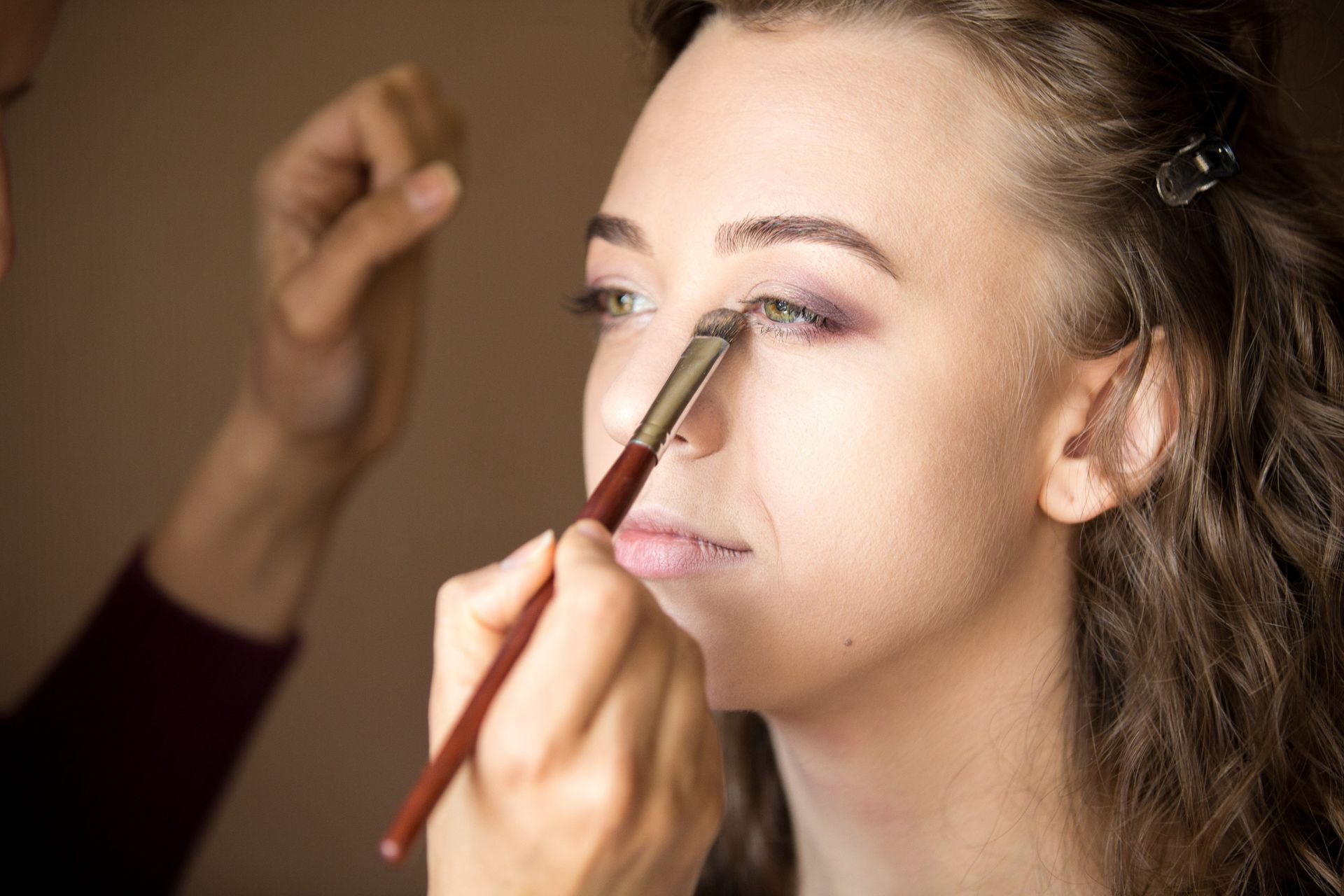 Makeup artist applying eyeshadow to a woman’s eyelid with a brush