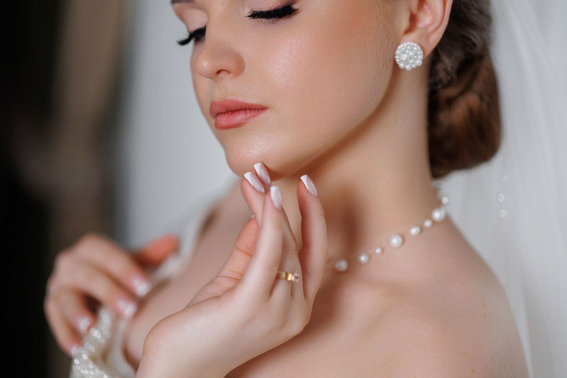 Close-up of a bride adjusting her necklace, wearing pearl earrings and soft makeup