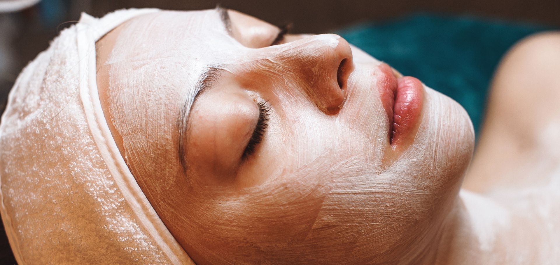 Close-up of a person receiving a white facial mask treatment while lying down with eyes closed