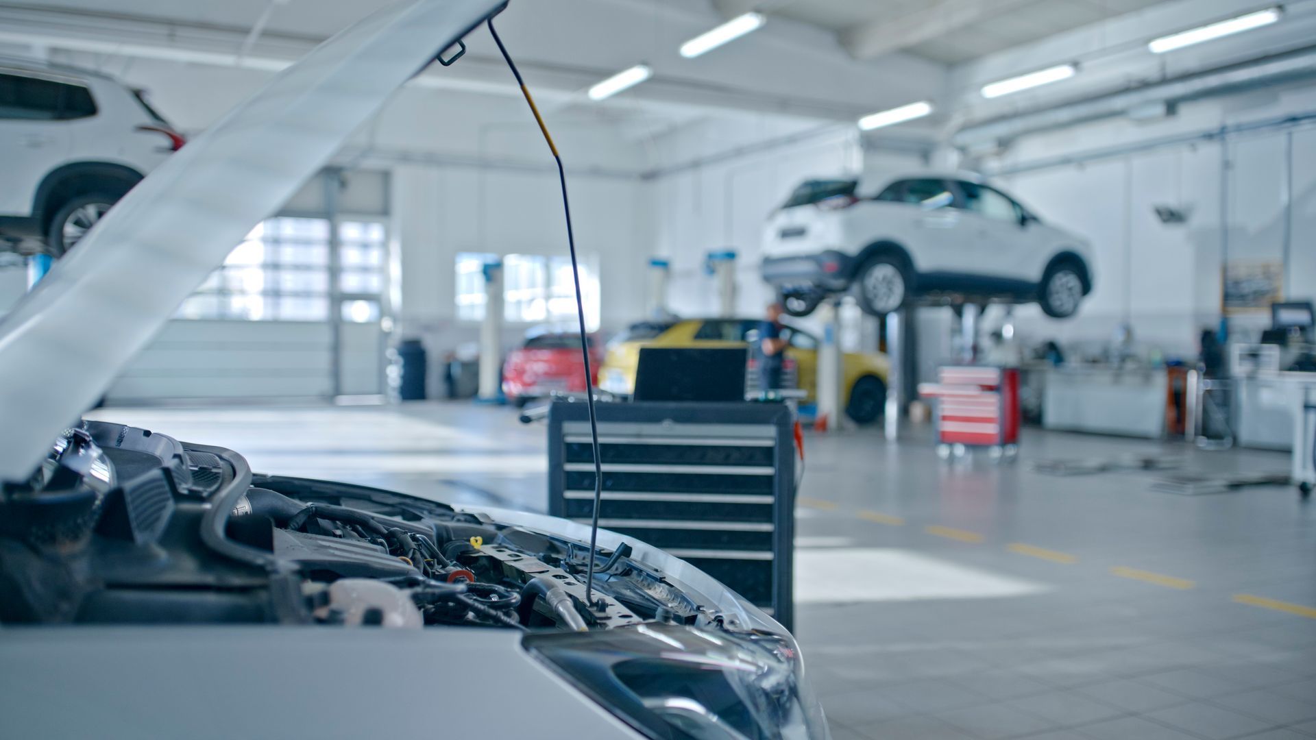 A car is being repaired in a garage with the hood open.