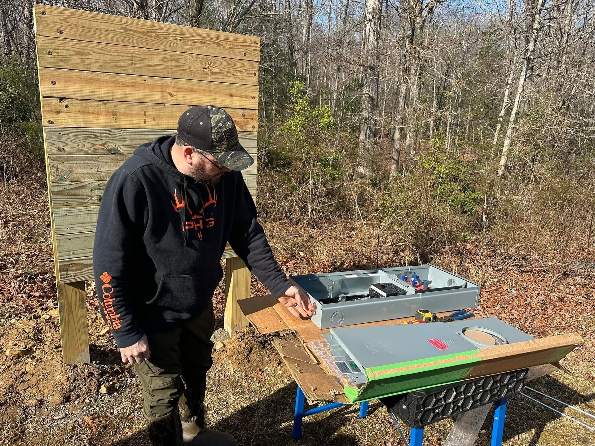 Person outdoors beside a table, pointing at a colorful board with targets and tools.