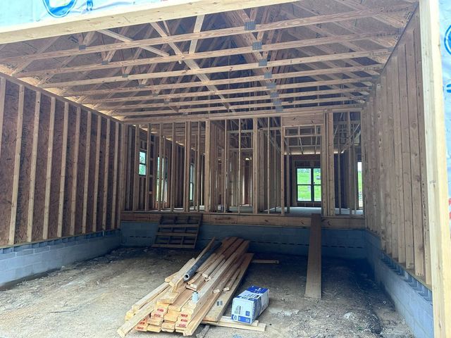 Unfinished wooden house interior with exposed framing, roof trusses, and construction materials on the floor