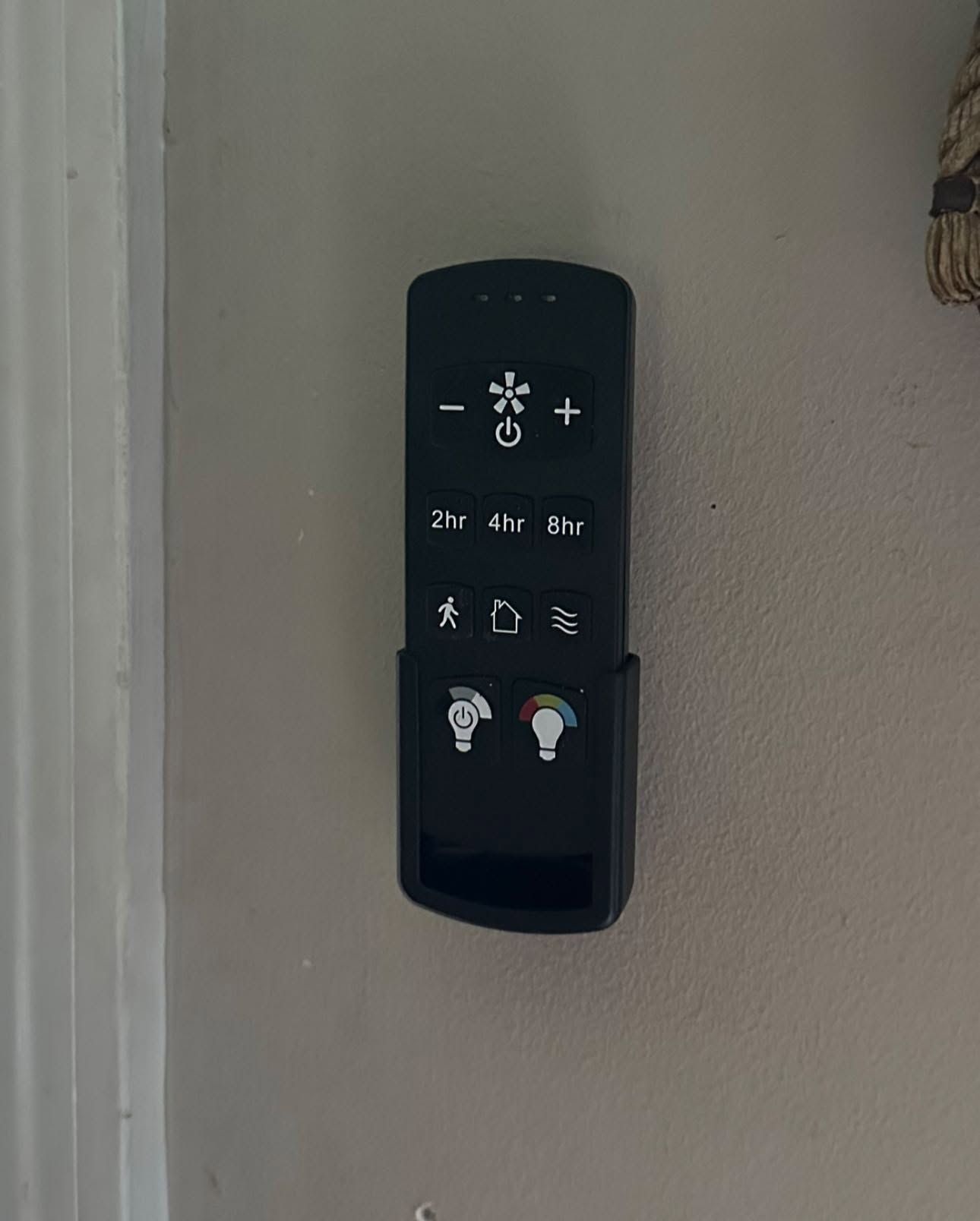Black wall-mounted remote control with light and fan buttons on a beige wall.