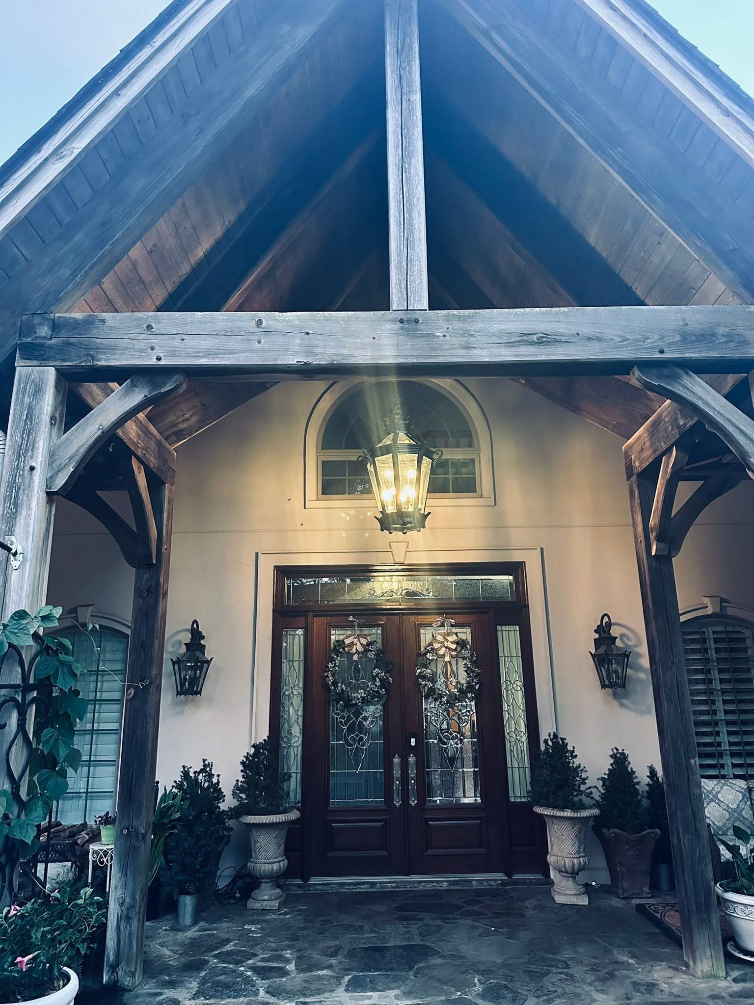 Rustic front entrance with wood beams, arched doorway, and glass double doors under a gabled porch