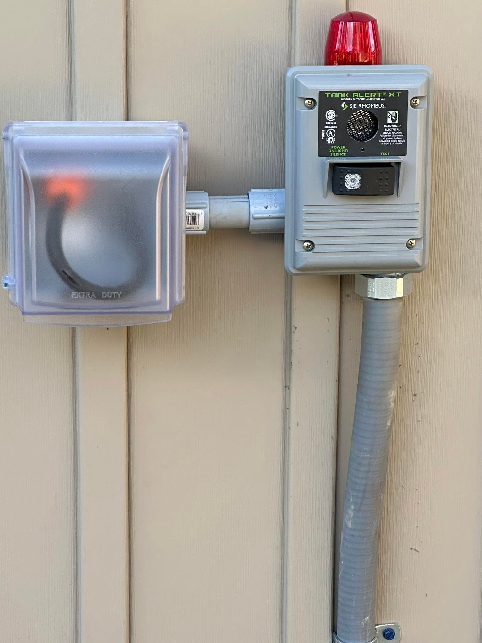 Outdoor electrical boxes and conduit mounted on a beige wall, one with a red beacon light.