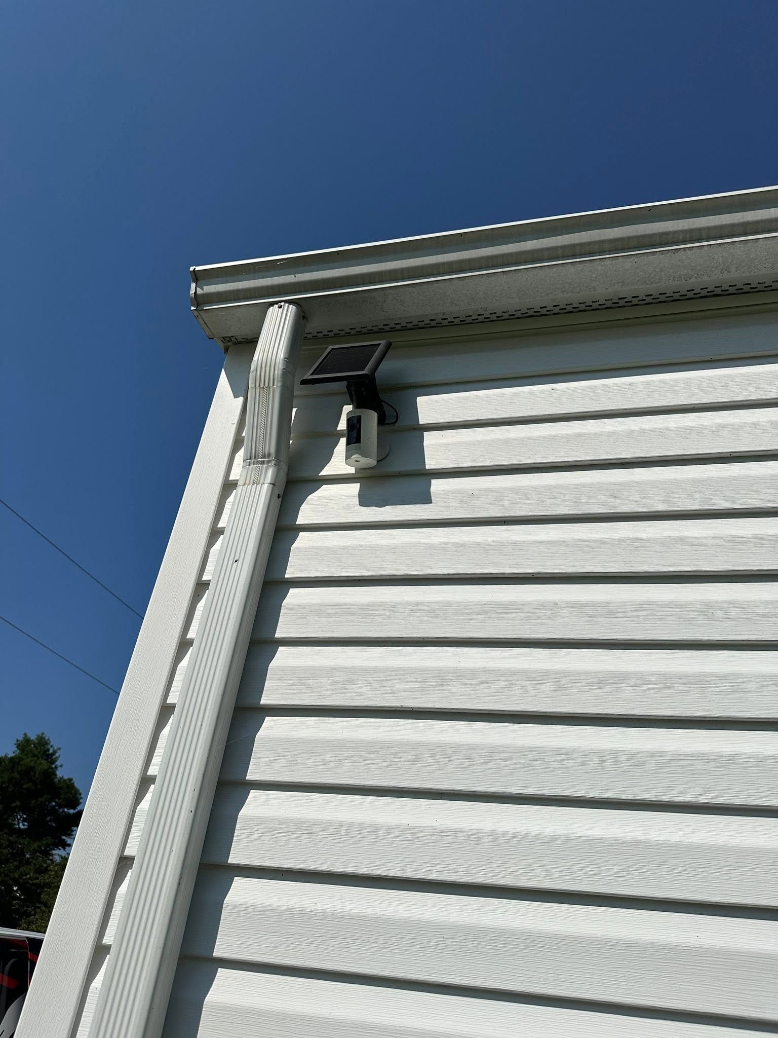 White house eave with rain gutter and downspout against a clear blue sky