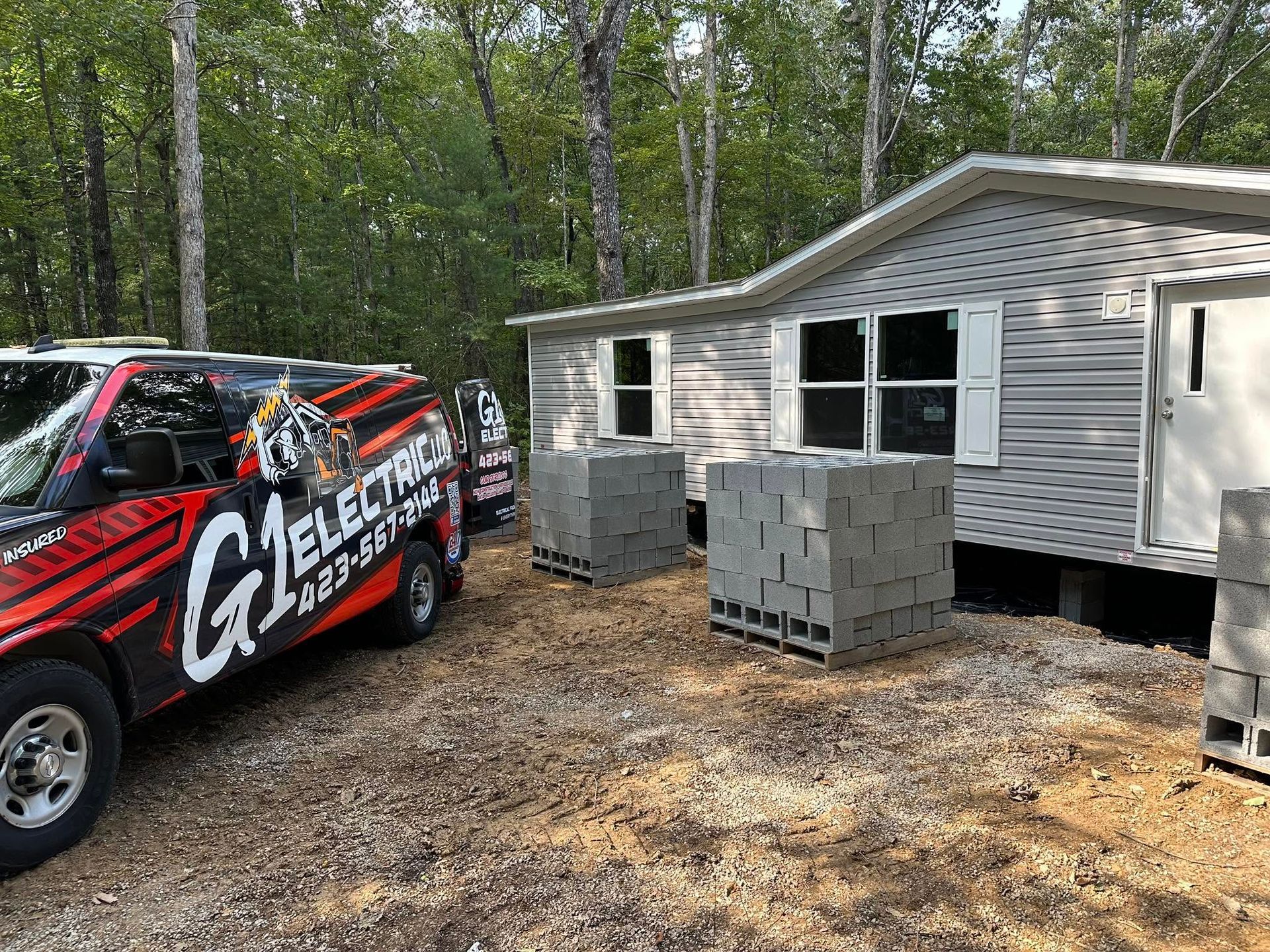 Mobile home under construction with work van and stacked cinder blocks in a wooded area