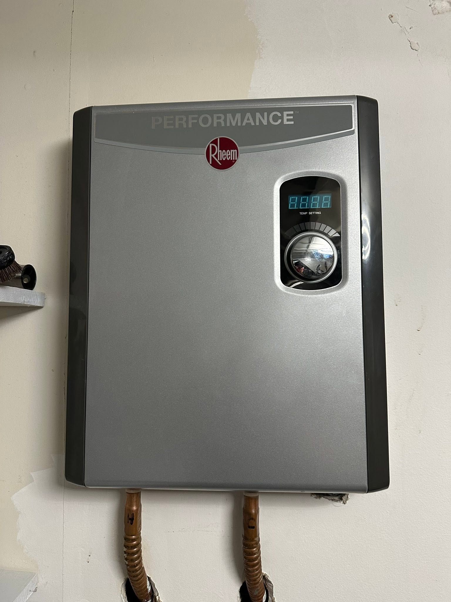 Wall-mounted gray water heater with a digital display and two copper pipes underneath.