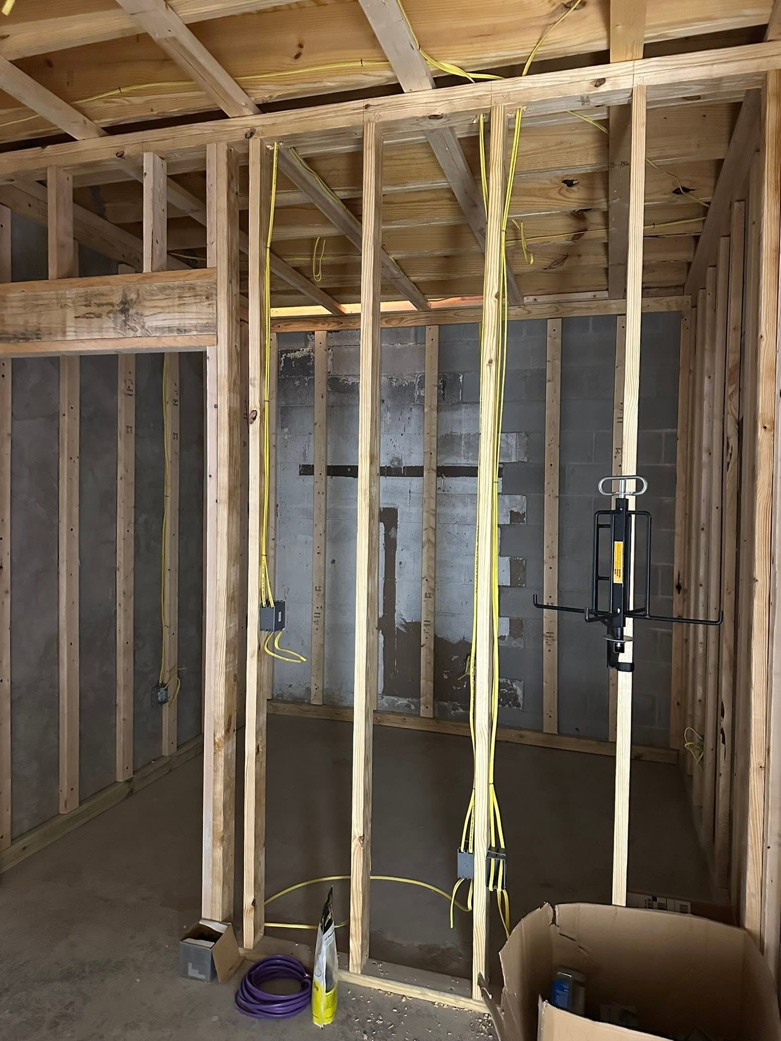 Framed basement wall with insulation, exposed studs, and hanging electrical wiring under construction